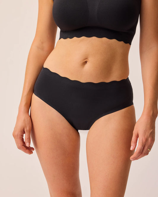 Model is wearing BareBond™ Cotton Maternity & Postpartum Brief in Black and BareBond™ Cotton Maternity & Nursing Bra in Black on a beige background. @model_info:KJ is wearing a Medium.