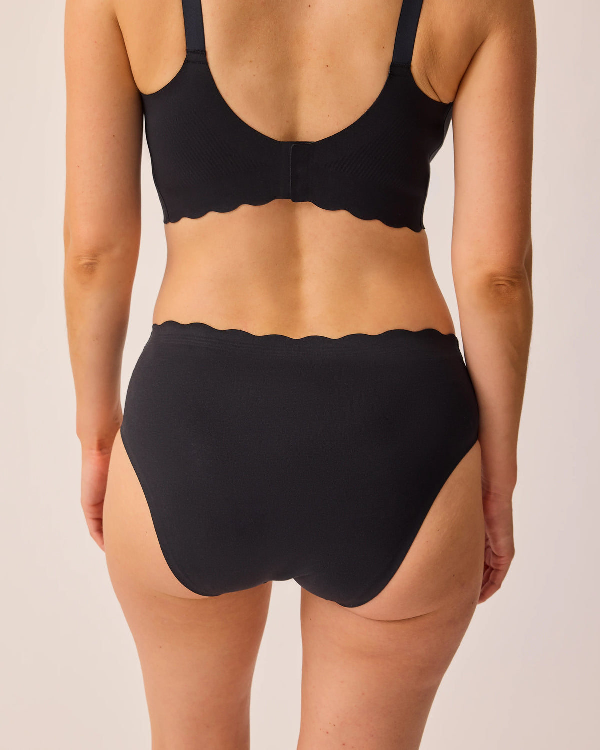 Back view of model wearing BareBond™ Cotton Maternity & Postpartum Brief in Black and BareBond™ Cotton Maternity & Nursing Bra in Black on a beige background.