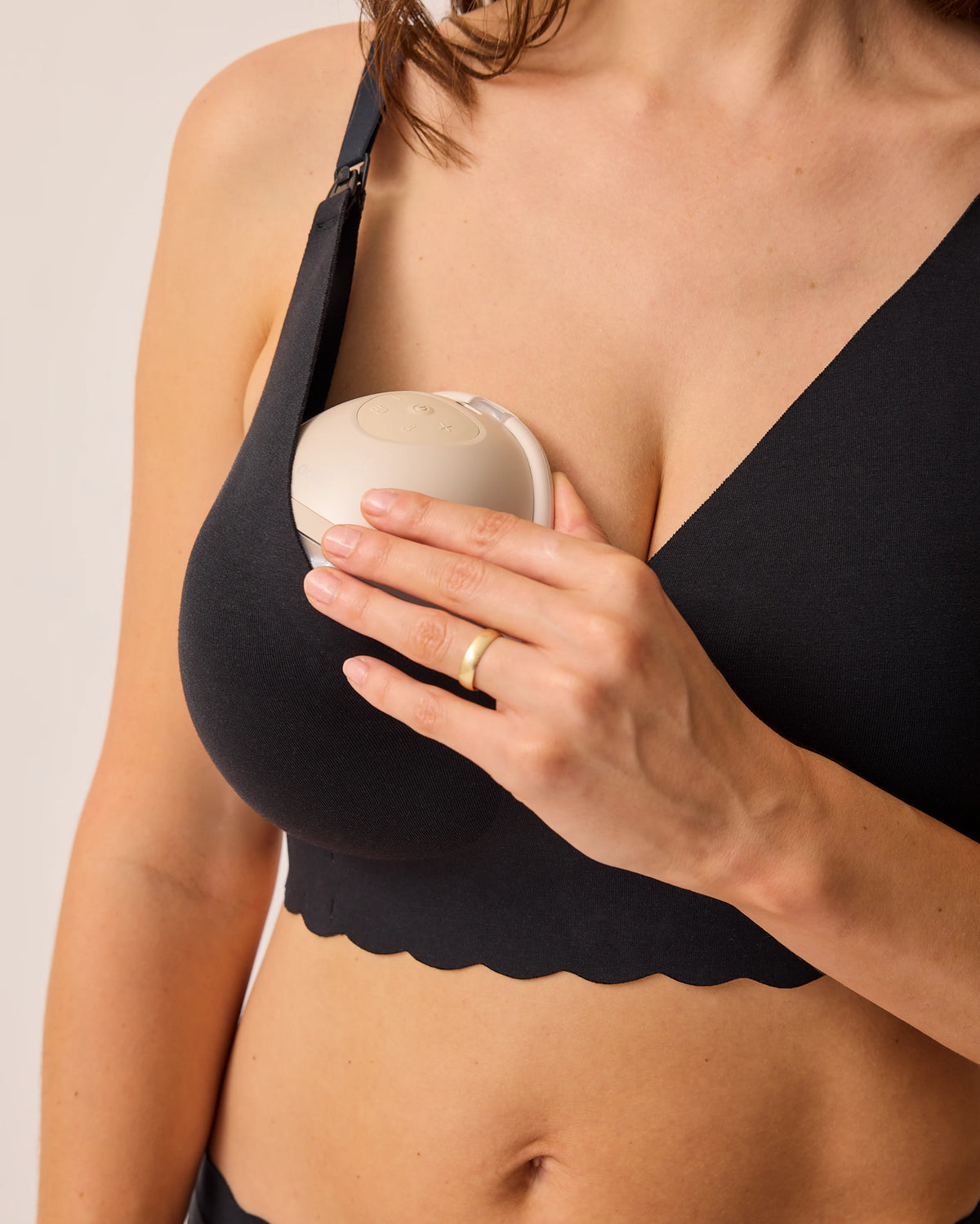 Model is holding mobile breast pump in BareBond™ Cotton Maternity & Nursing Plunge Bra in Black on a beige background.