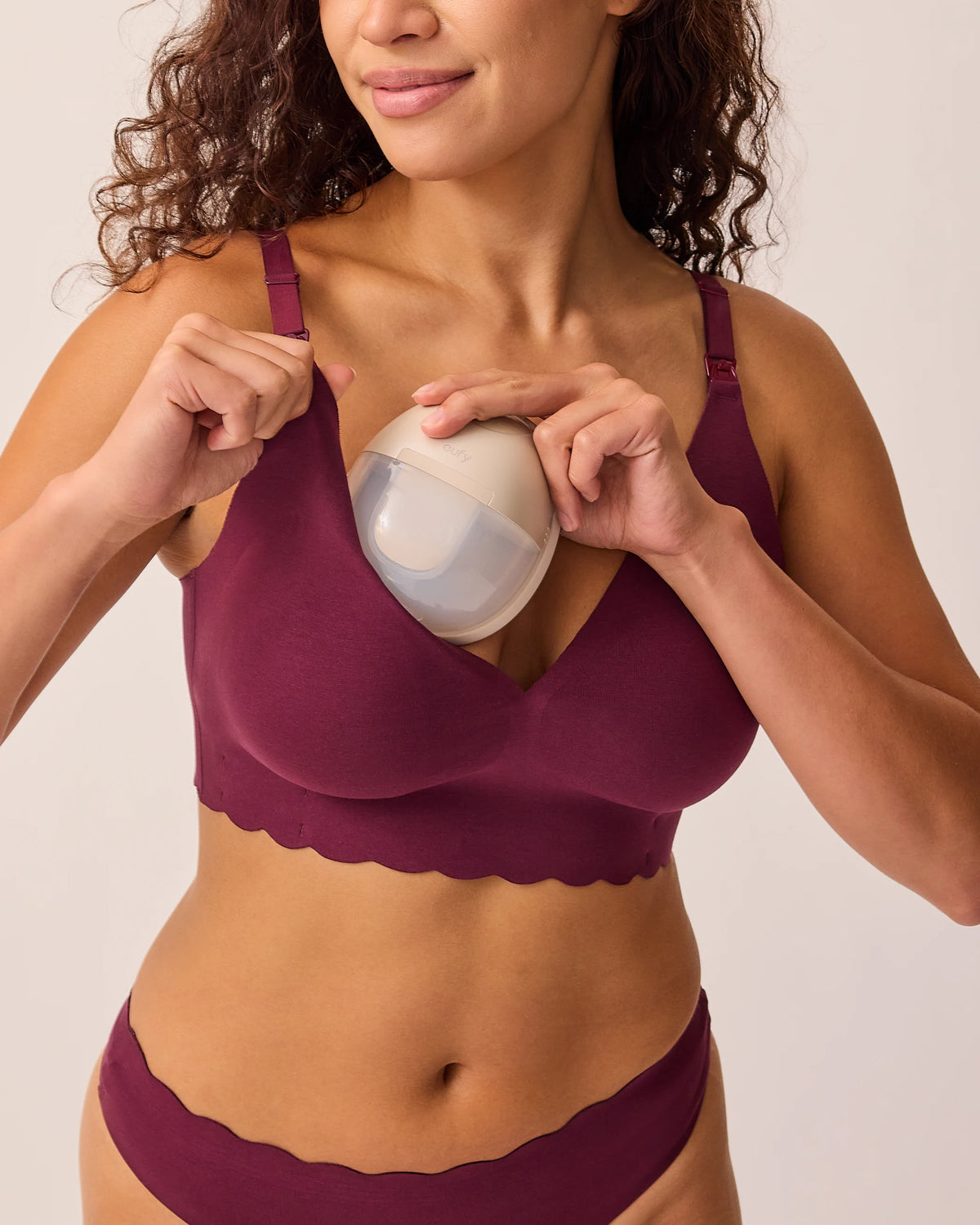 Model is placing mobile pumps while wearing BareBond™ Cotton Maternity & Nursing Plunge Bra in Garnet  and BareBond™ Cotton Maternity & Postpartum Thong in Garnet on a beige background.