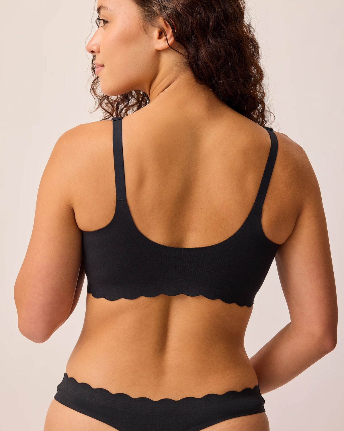 Back view of model wearing BareBond™ Cotton Maternity & Nursing Bralette and BareBond™ Cotton Maternity & Postpartum Thong in Black on a beige background.