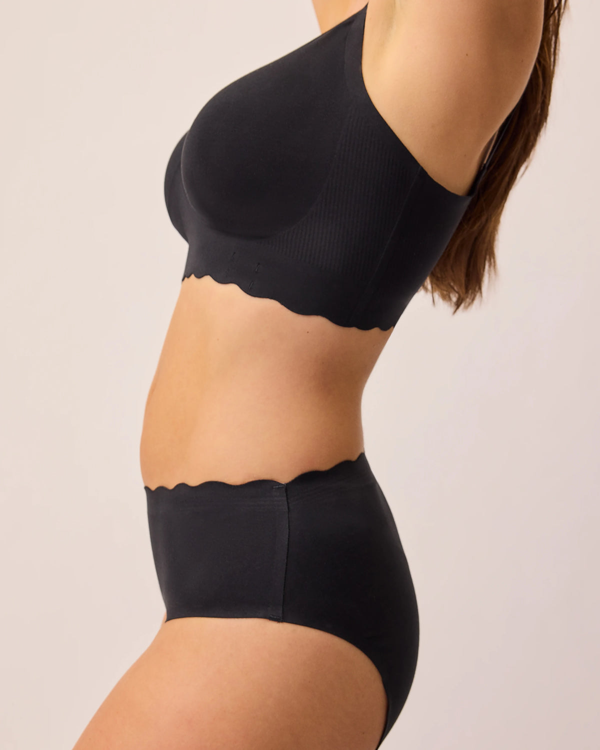 Side view of model wearing BareBond™ Cotton Maternity & Nursing Plunge Bra and BareBond™ Cotton Maternity & Postpartum Hipster in Black on a beige background.