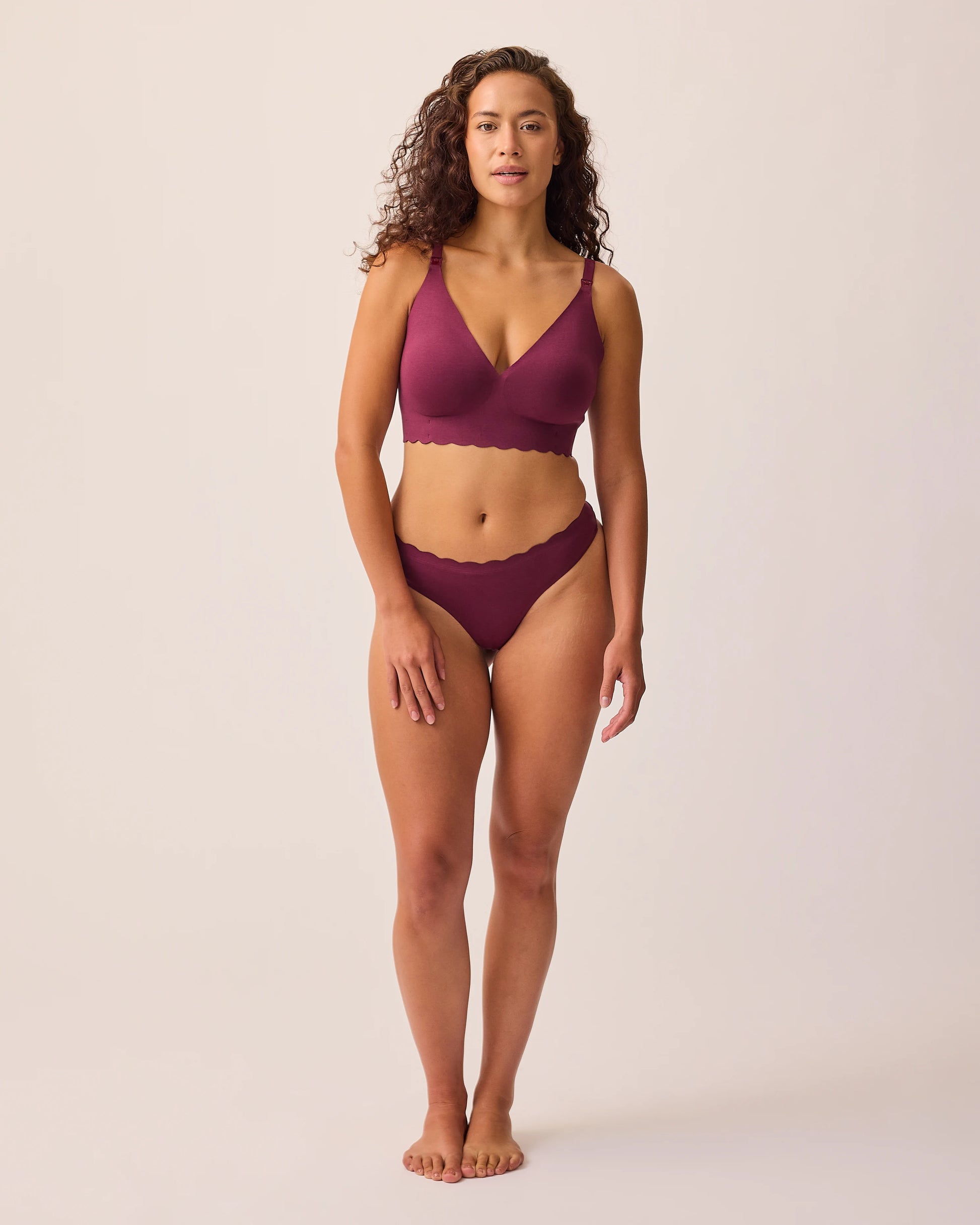 Model is wearing BareBond™ Cotton Maternity & Postpartum Thong in Garnet and BareBond™ Cotton Maternity & Nursing Plunge Bra in Garnet on a beige background. 