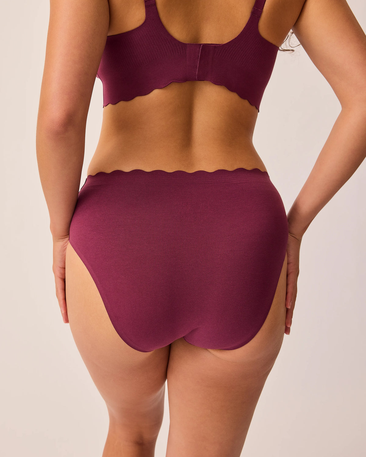 Back view of model wearing BareBond™ Cotton Maternity & Postpartum Brief in Garnet and BareBond™ Cotton Maternity & Nursing Plunge Bra in Garnet on a beige background. 