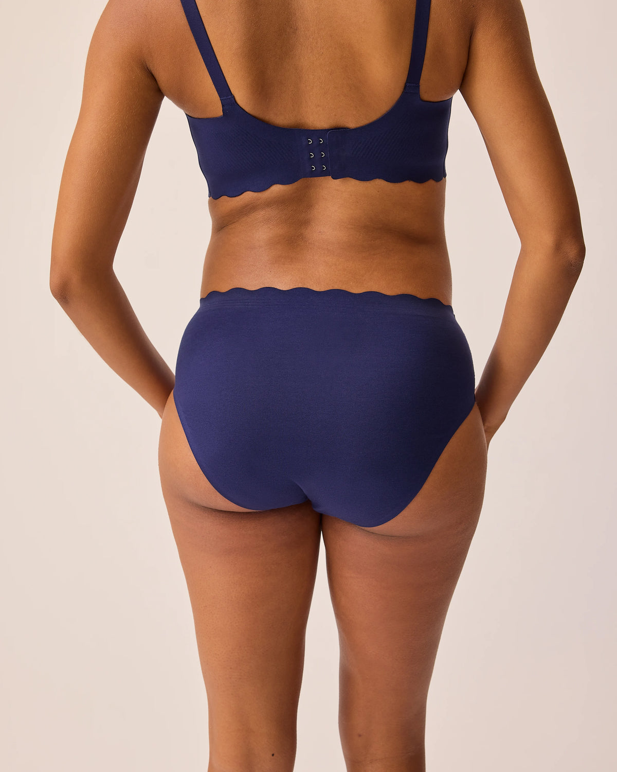 Back view of model wearing BareBond™ Cotton Maternity & Postpartum Hipster in Coastal Navy and BareBond™ Cotton Maternity & Nursing Plunge Bra in Coastal Navy on a beige background. 