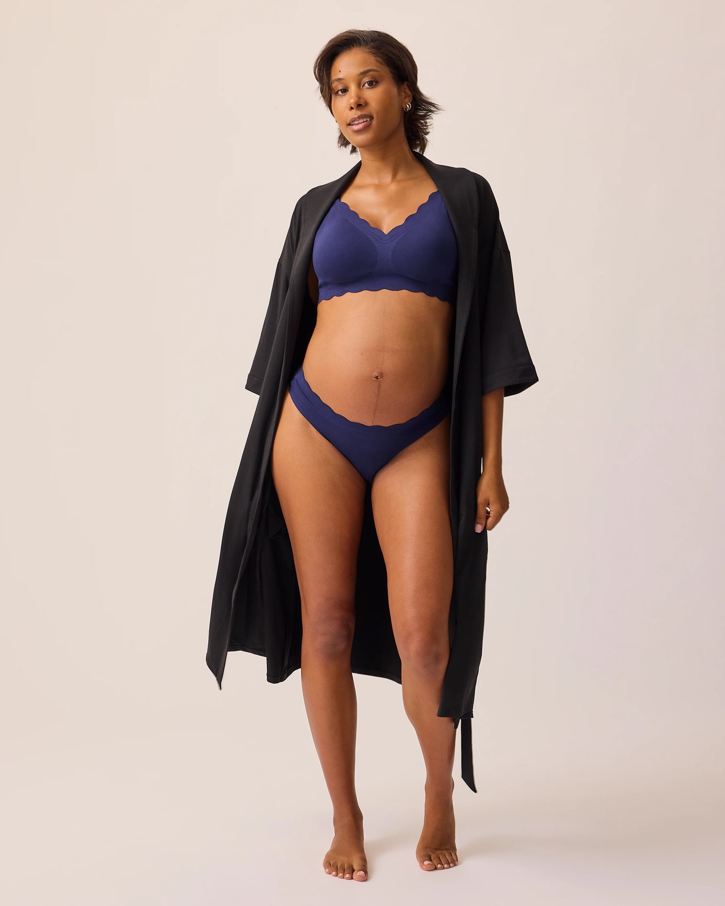 Model is wearing BareBond™ Cotton Maternity & Postpartum Thong in Coastal Navy and BareBond™ Cotton Maternity & Nursing Bra in Coastal Navy  topped with a The Restore Cotton Blend Robe in Black, on a beige background. 