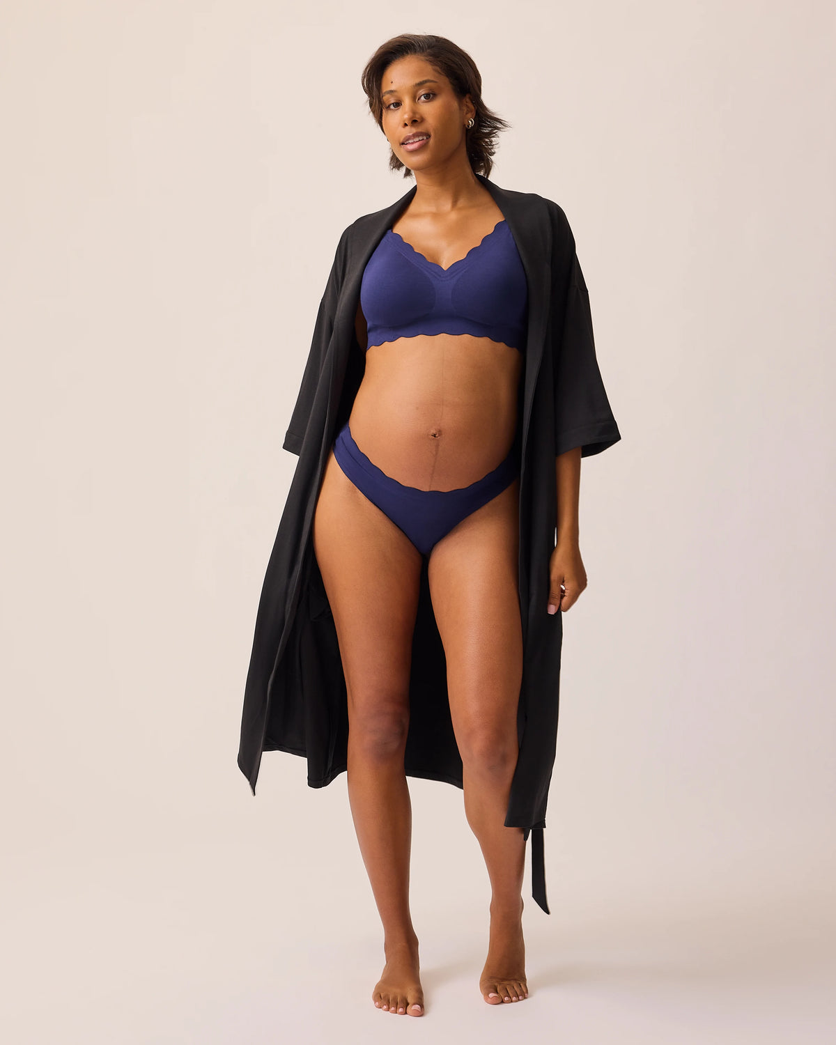 Model is wearing BareBond™ Cotton Maternity & Postpartum Thong in Coastal Navy and BareBond™ Cotton Maternity & Nursing Bra in Coastal Navy  topped with a The Restore Cotton Blend Robe in Black, on a beige background. 