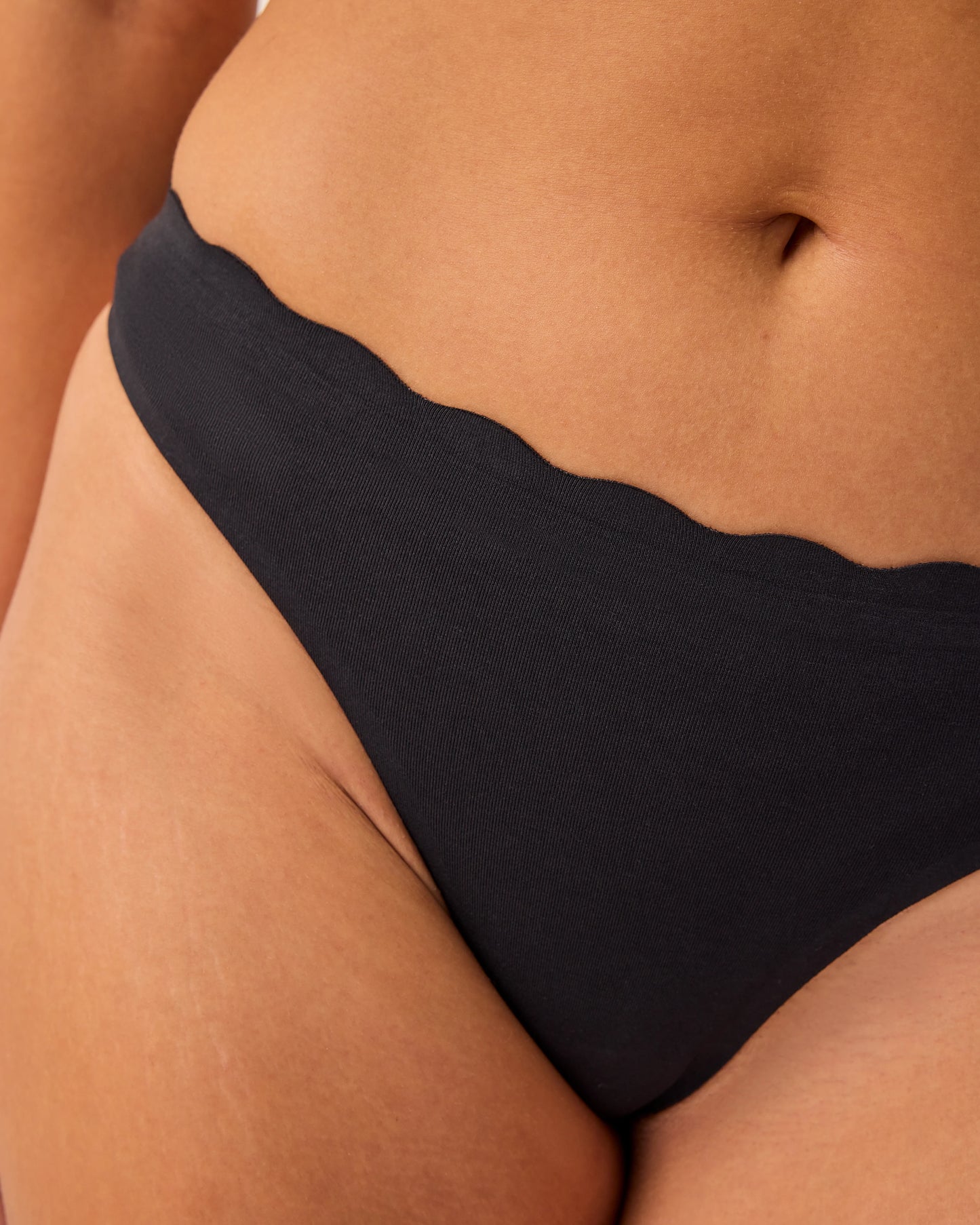 Close up of model wearing BareBond™ Cotton Maternity & Postpartum Thong in Black on a beige background. 