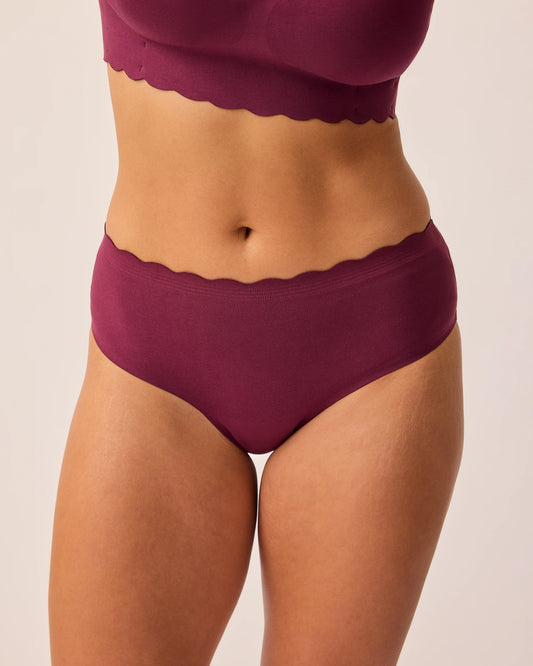 Close up of model wearing BareBond™ Cotton Maternity & Postpartum Brief in Garnet and BareBond™ Cotton Maternity & Nursing Plunge Bra in Garnet on a beige background.  @model_info:Sadie is wearing a Medium.
