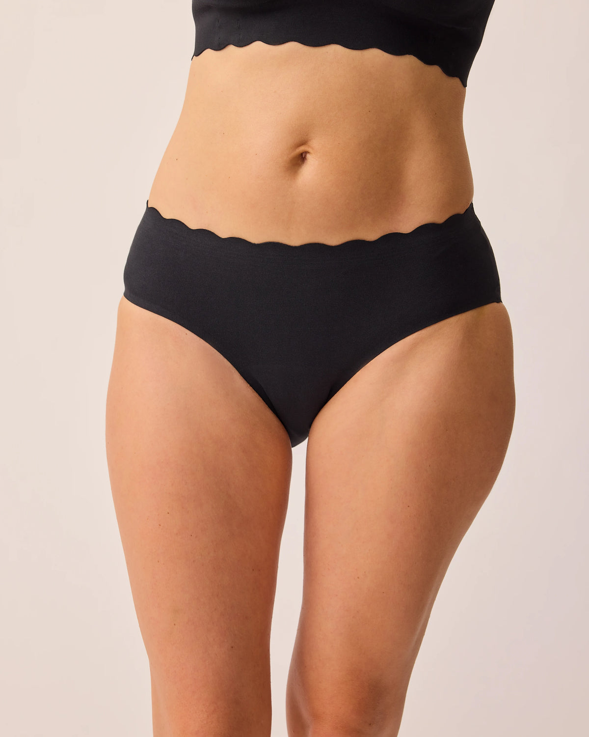 Model is wearing BareBond™ Cotton Maternity & Postpartum Hipster in Black and BareBond™ Cotton Maternity & Nursing Bra in Black on a beige background. @model_info:KJ is wearing a Medium.