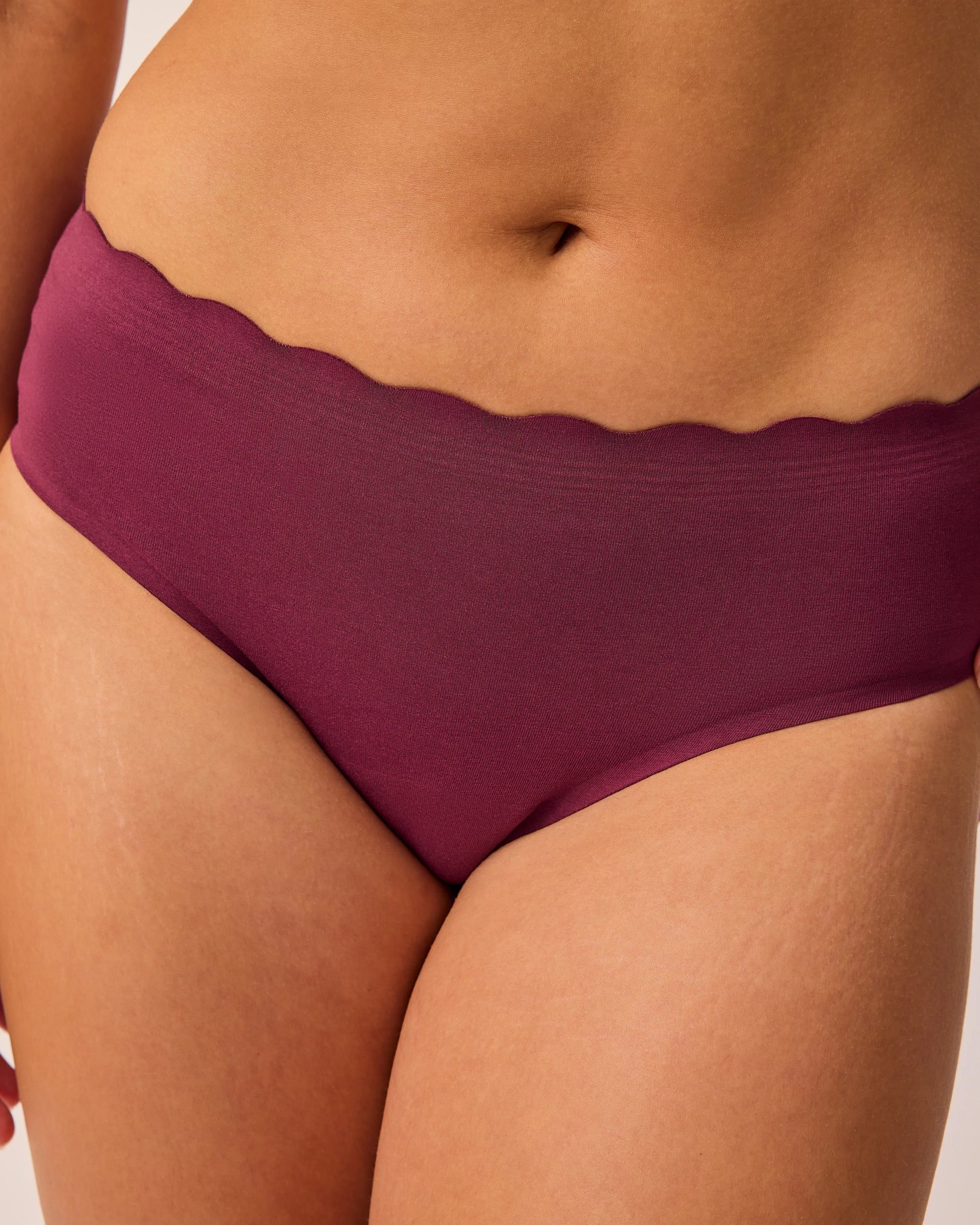 Close up of model wearing BareBond™ Cotton Maternity & Postpartum Hipster in Garnet on a beige background.