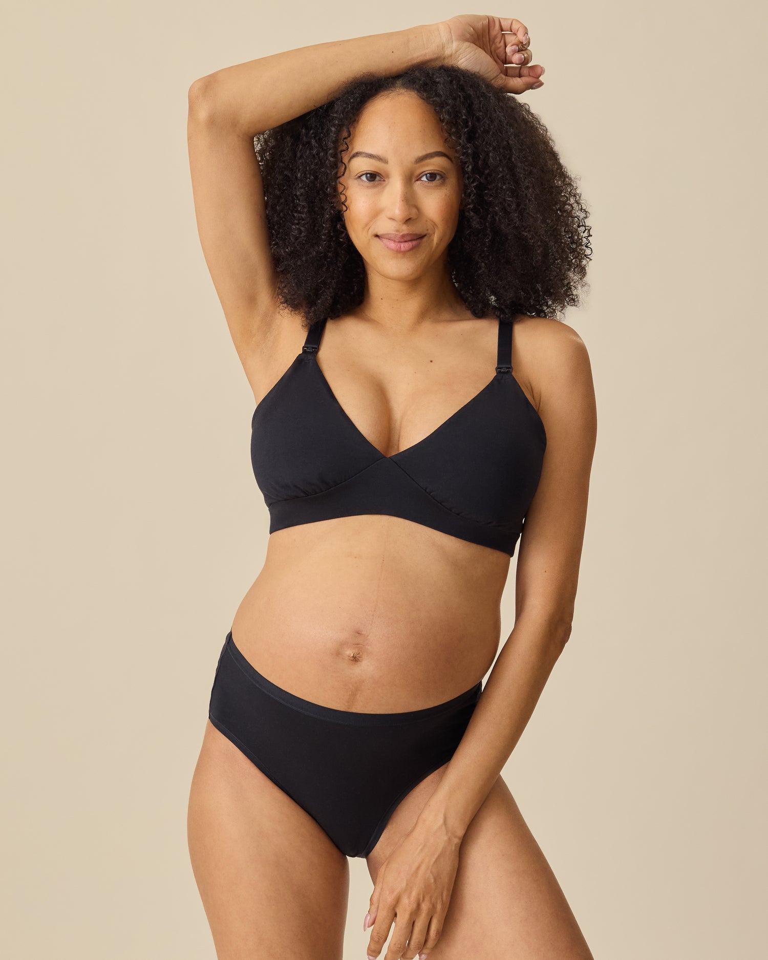Model is wearing SoftStretch Cotton Maternity & Nursing Bralette in Black and SoftStretch Cotton Maternity & Postpartum Brief in Black on a beige background.