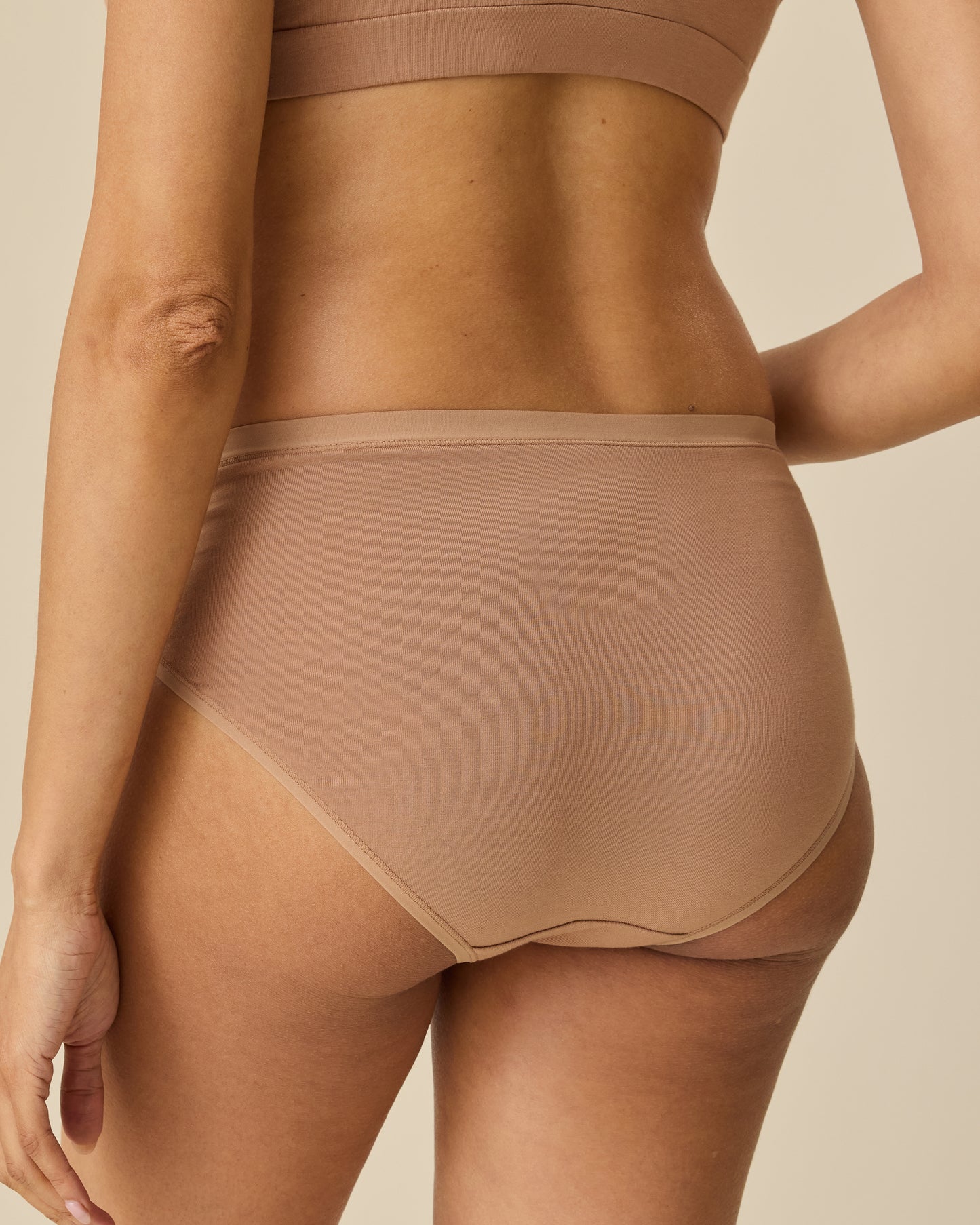 Back view of model wearing SoftStretch Cotton Maternity & Postpartum Hipster in Buff, on a beige background.