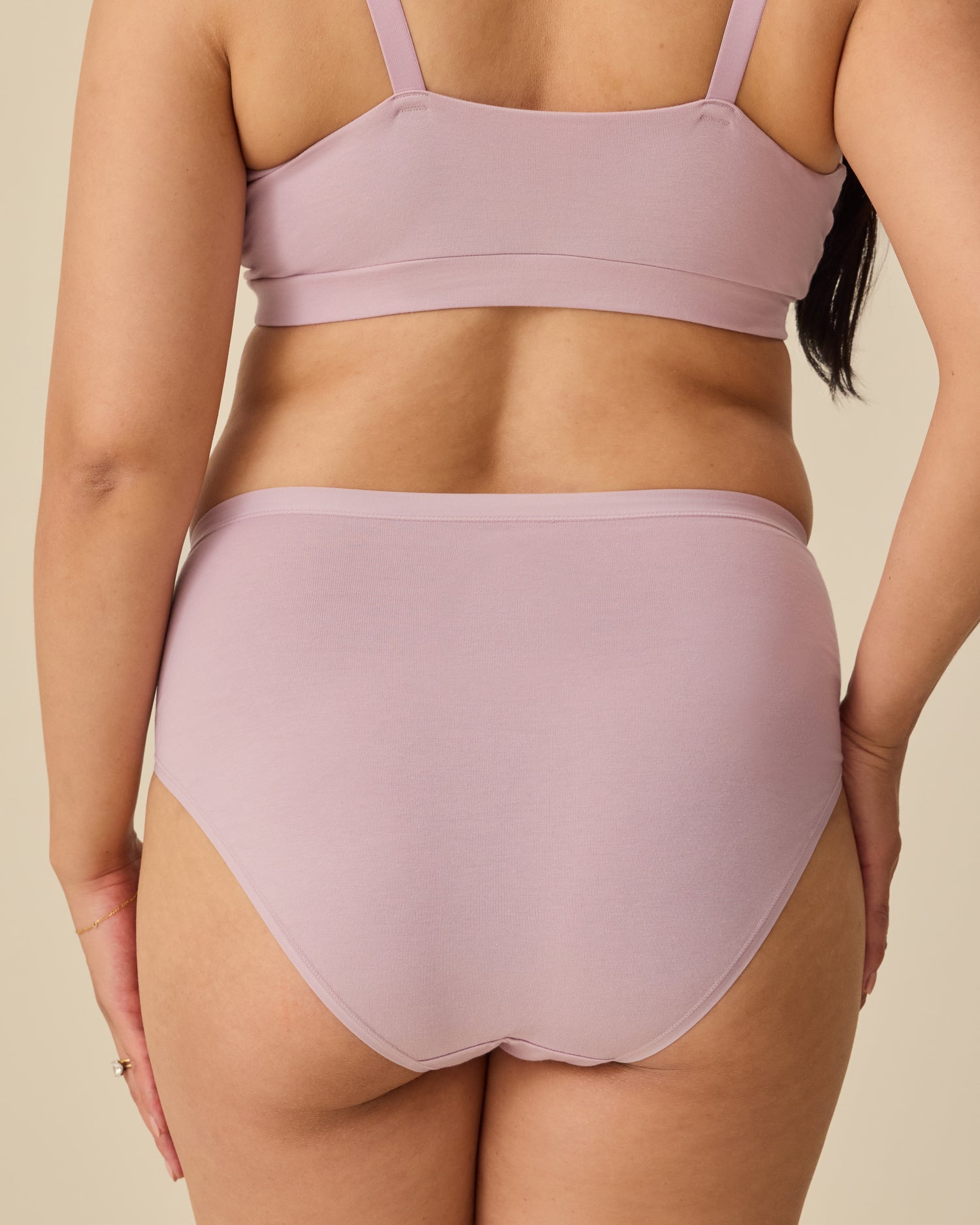 Back view of the model wearing SoftStretch Cotton Maternity & Nursing Bralette in Lilac Mist  and SoftStretch Cotton Maternity & Postpartum Hipster in Lilac Mist on a beige background. 