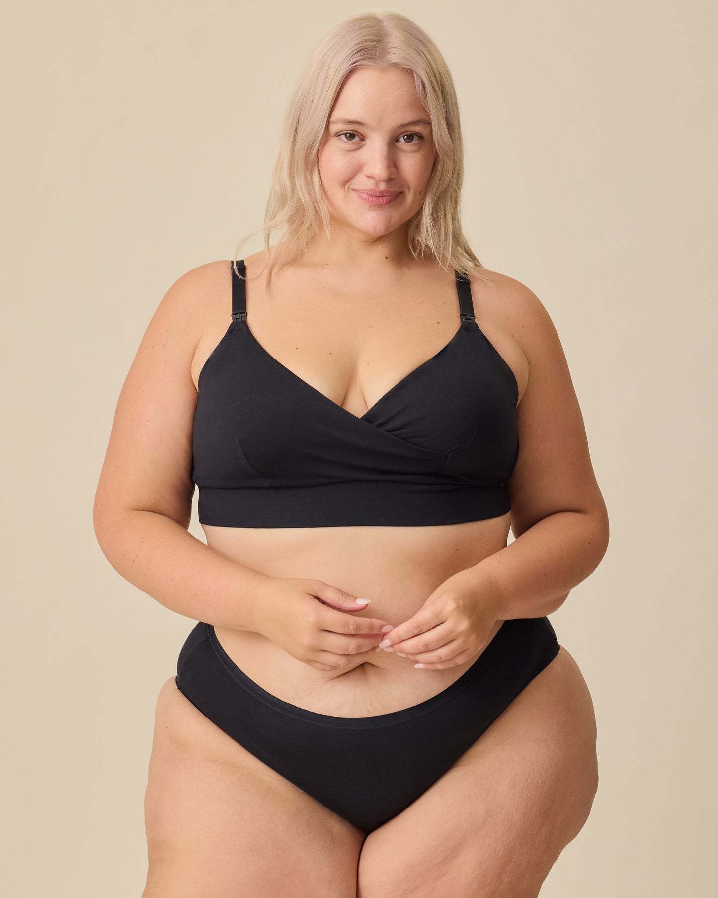 Model is wearing SoftStretch Cotton Nursing Bra in Black and SoftStretch Cotton Maternity & Postpartum Hipster in Black on a beige background.