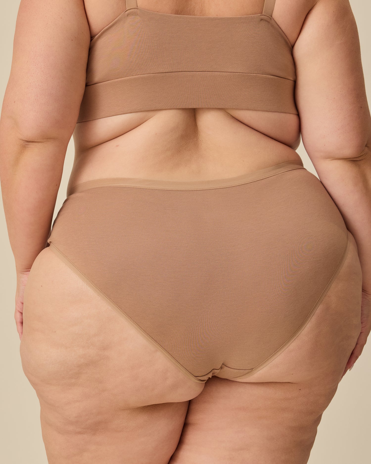 Back view of model wearing SoftStretch Cotton Nursing Bra in Buff and SoftStretch Cotton Maternity & Postpartum Brief in Buff on a beige background.