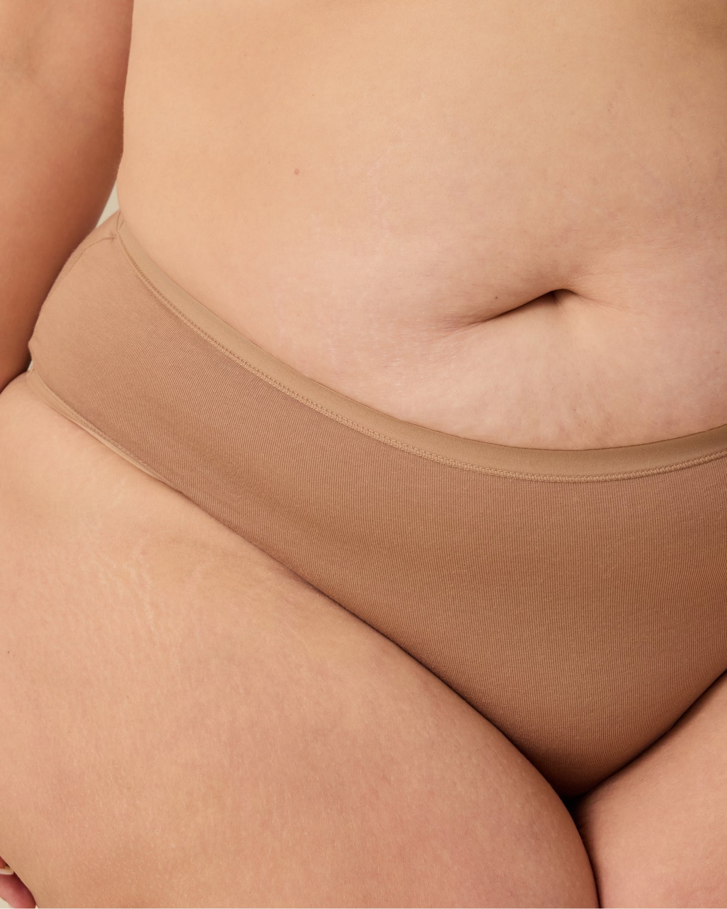 Close up of model wearing SoftStretch Cotton Maternity & Postpartum Brief in Buff on a beige background.@model_info:Allie is wearing a 1X.