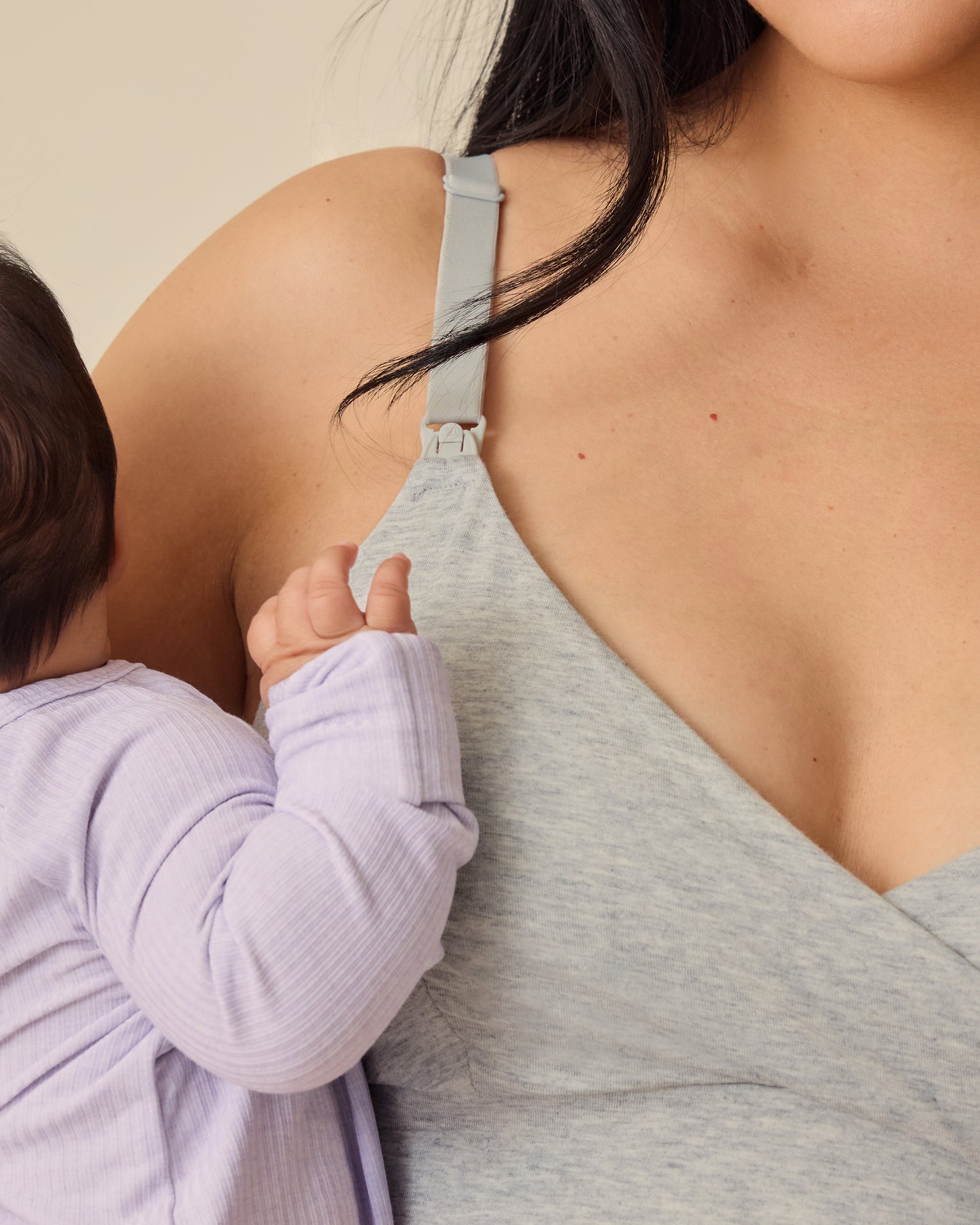 Mother holding baby in Ribbed Bamboo Baby Pajama in Lilac Heather, while wearing SoftStretch Cotton Nursing Bra in Grey Heather, on a beige background.