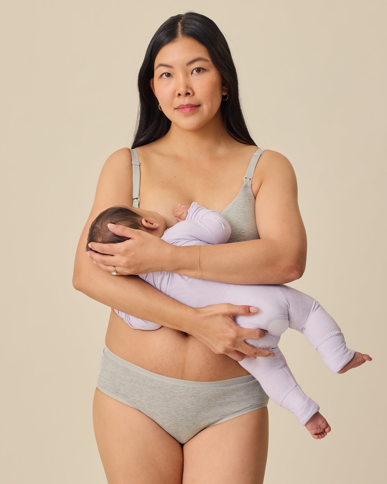 Mother nursing baby in Ribbed Bamboo Baby Pajama in Lilac Heather, while wearing SoftStretch Cotton Nursing Bra and SoftStretch Cotton Maternity & Postpartum Hipster in Grey Heather on a beige background. 