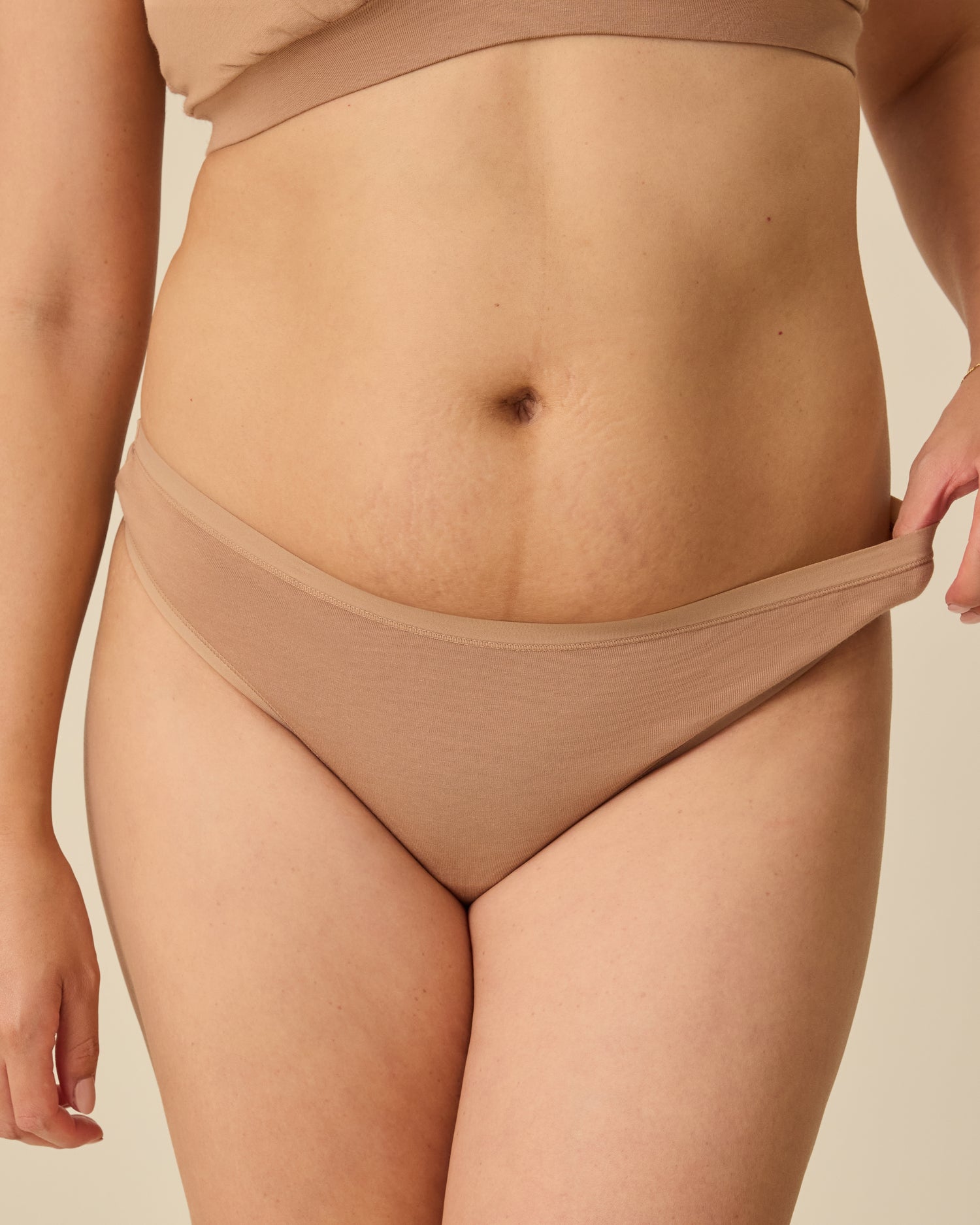 Close up of model wearing the SoftStretch Cotton Maternity & Nursing Bralette in Buff and SoftStretch Cotton Maternity & Postpartum Thong in Buff, on a beige background. @model_info:Theresa is wearing a Small.