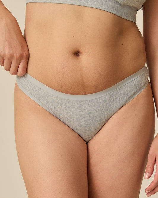 Model wearing the SoftStretch Cotton Maternity & Nursing Bralette in Grey Heather and SoftStretch Cotton Maternity & Postpartum Thong in Grey Heather, on a beige background.@model_info:Theresa is wearing a Small.