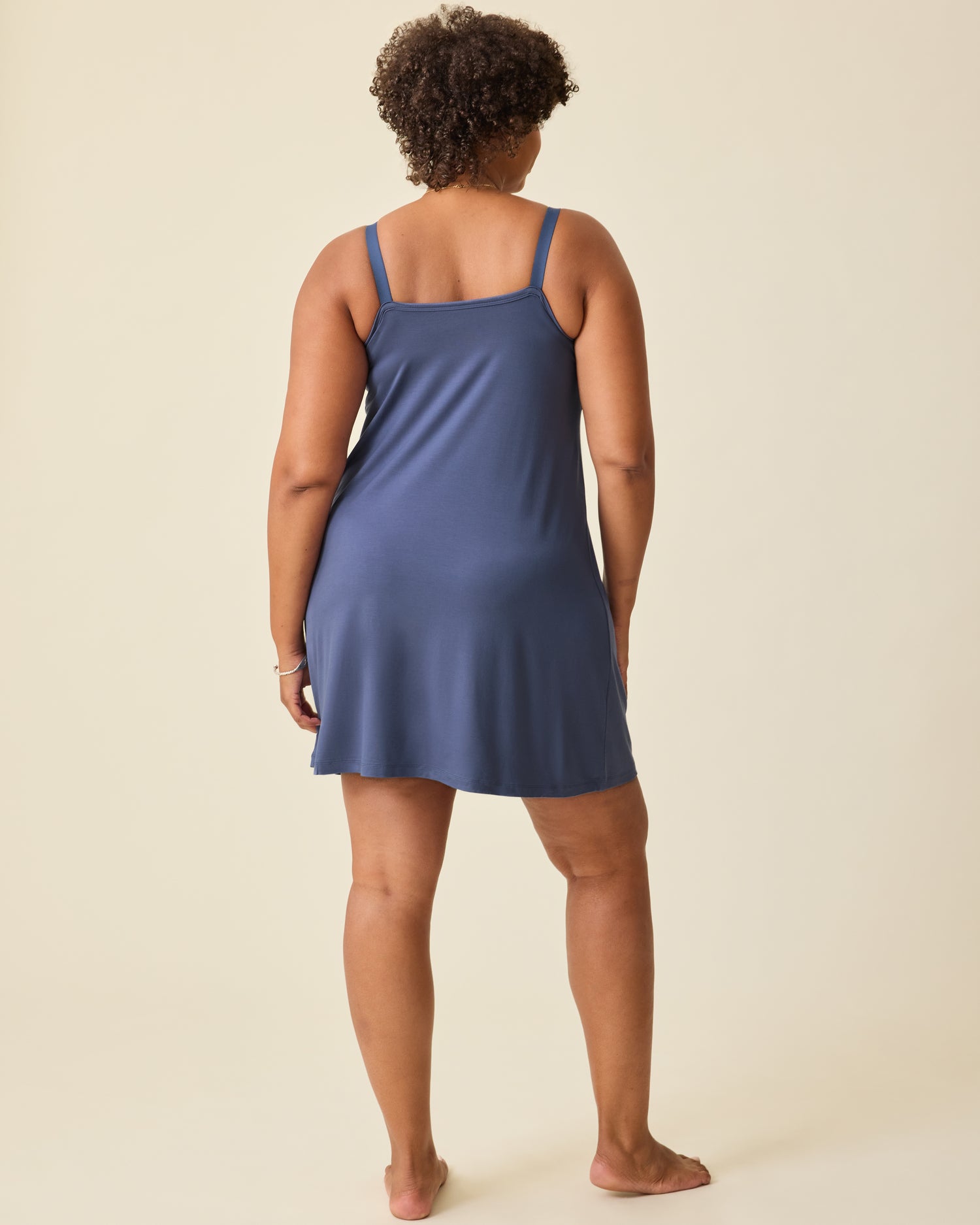 Back view of model wearing Stella Hands-Free Pumping & Nursing Nightgown in Slate Blue, on a beige background.