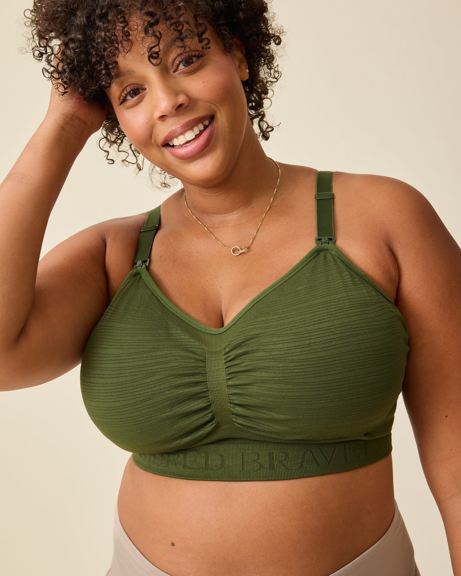 Model is wearing Sublime® Hands-Free Pumping & Nursing Bra in Deep Olive on a beige background. @model_info:Skye is wearing a Busty X-Large.