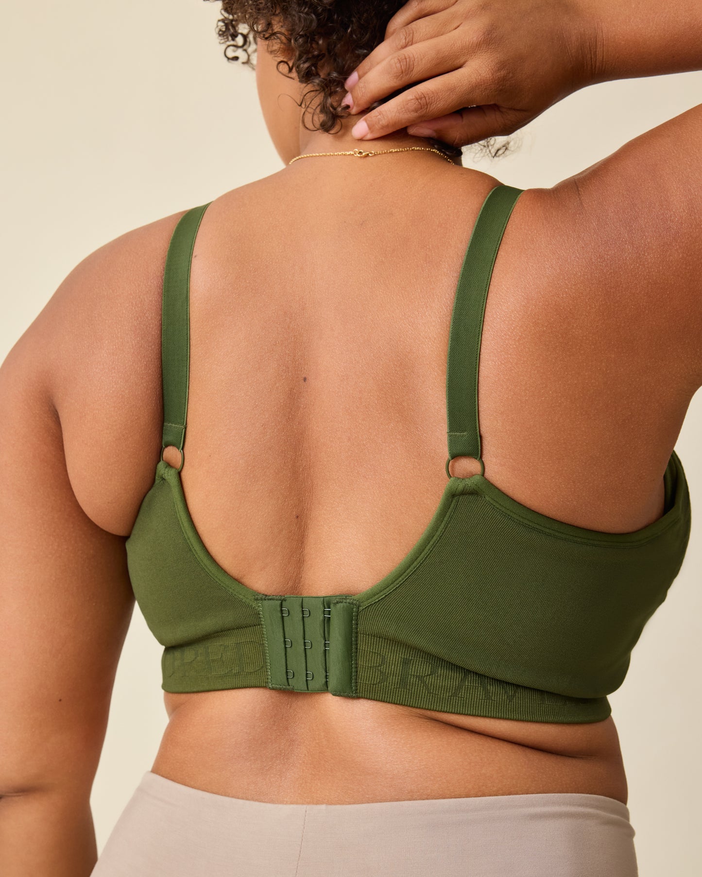 Back view of model wearing Sublime® Hands-Free Pumping & Nursing Bra in Deep Olive on a beige background.