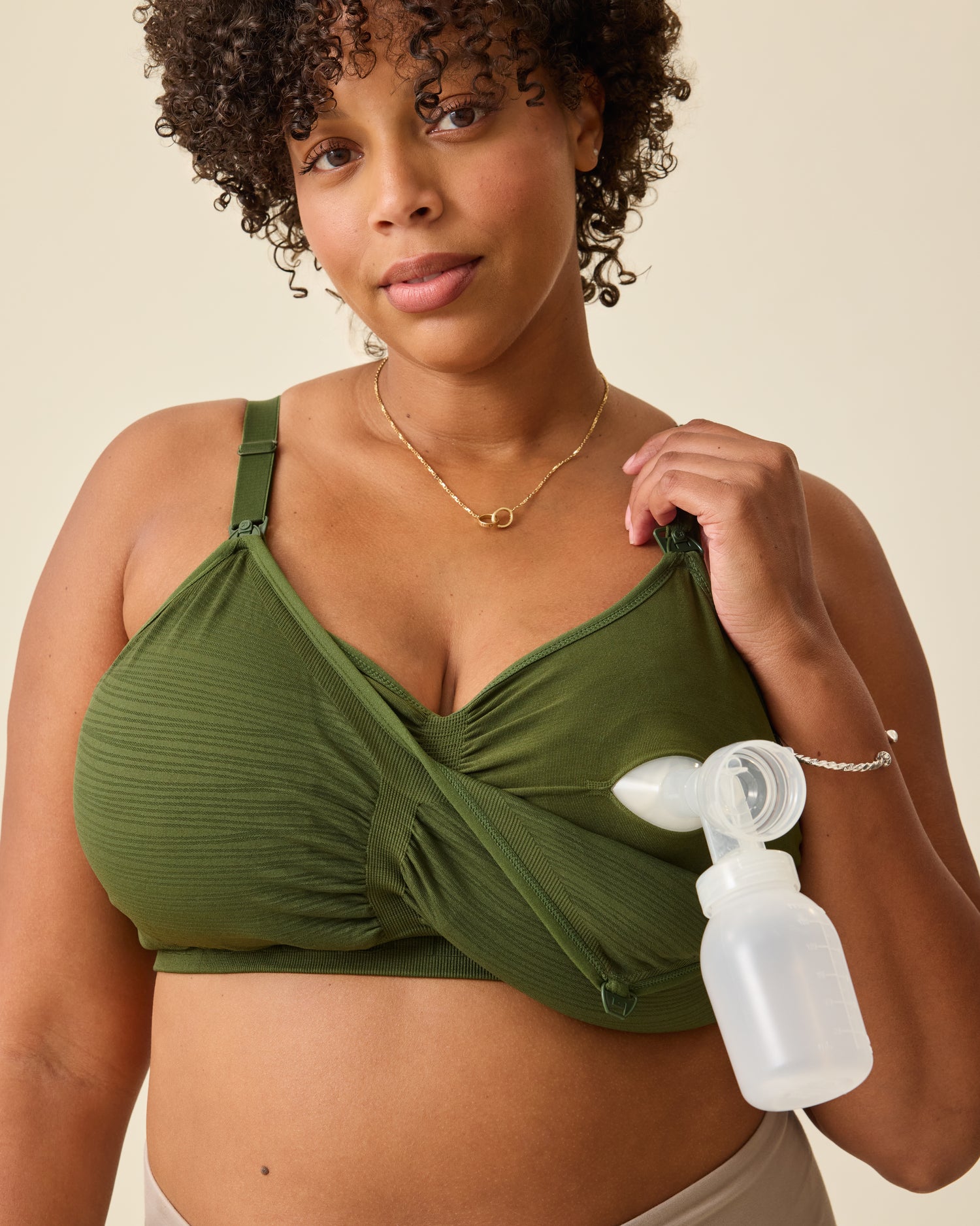 Model is displaying pumping access in Sublime® Hands-Free Pumping & Nursing Bra in Deep Olive on a beige background.