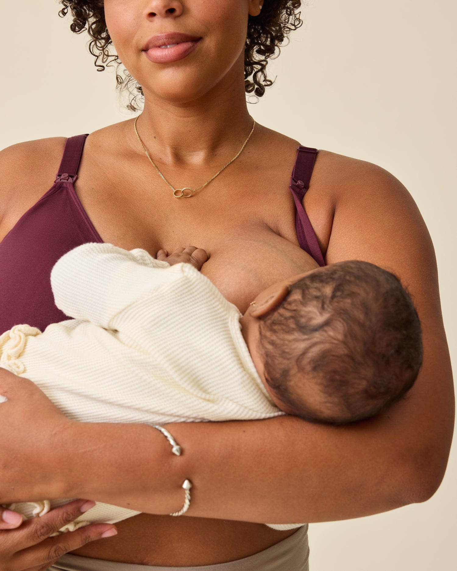 Model is breastfeeding while wearing Simply Sublime® Nursing Bra in Deep Burgundy, on a beige background.