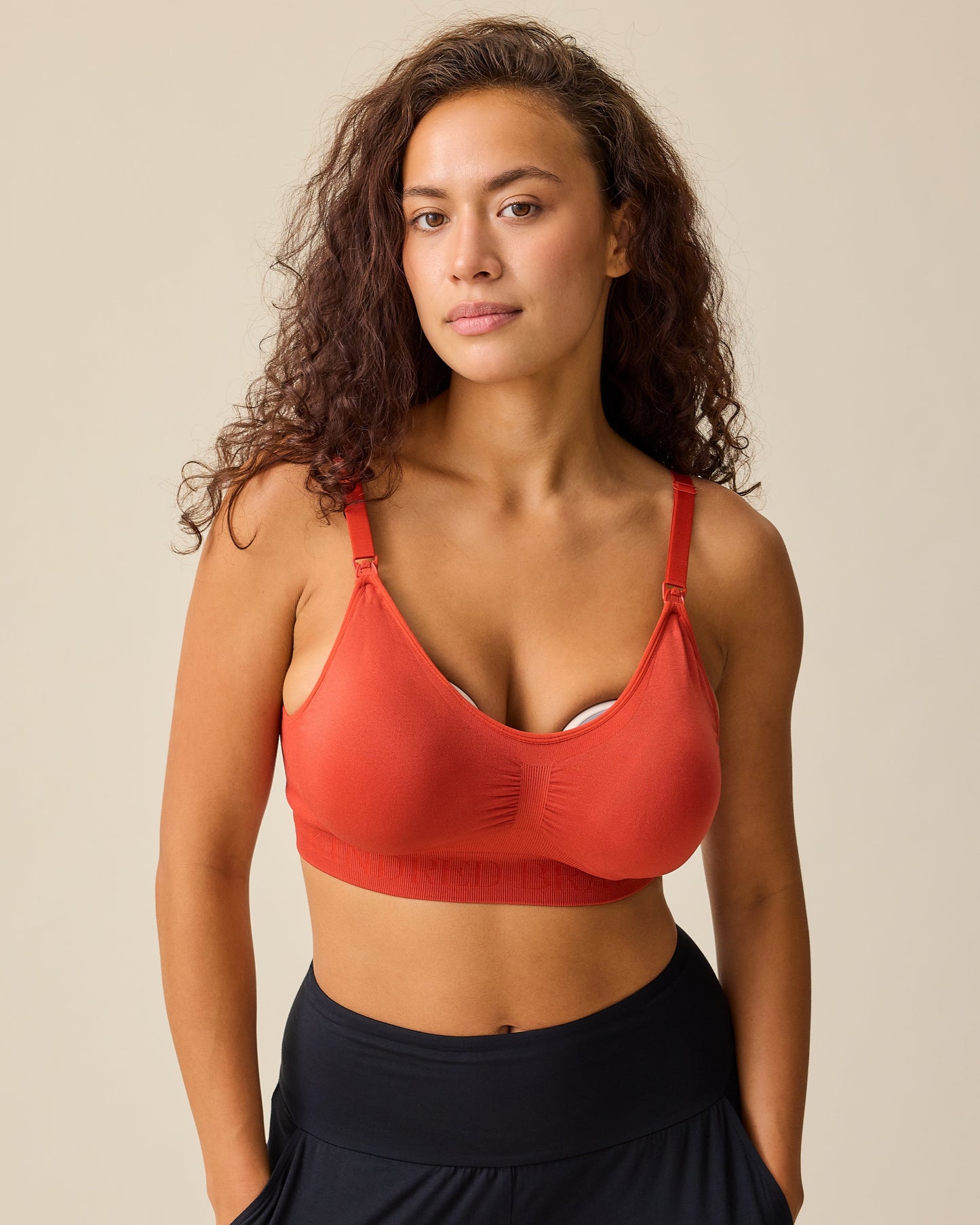 Model is wearing Simply Sublime® Nursing Bra in Spice while pumping, on a beige background. 