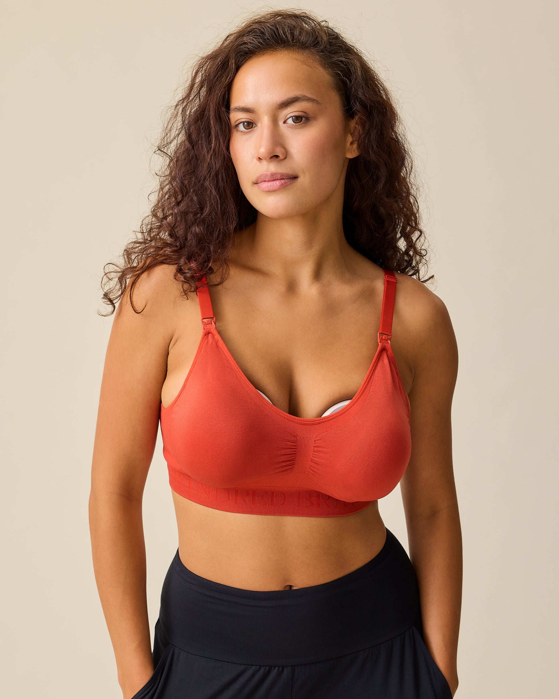 Model is wearing Simply Sublime® Nursing Bra in Spice while pumping, on a beige background. 