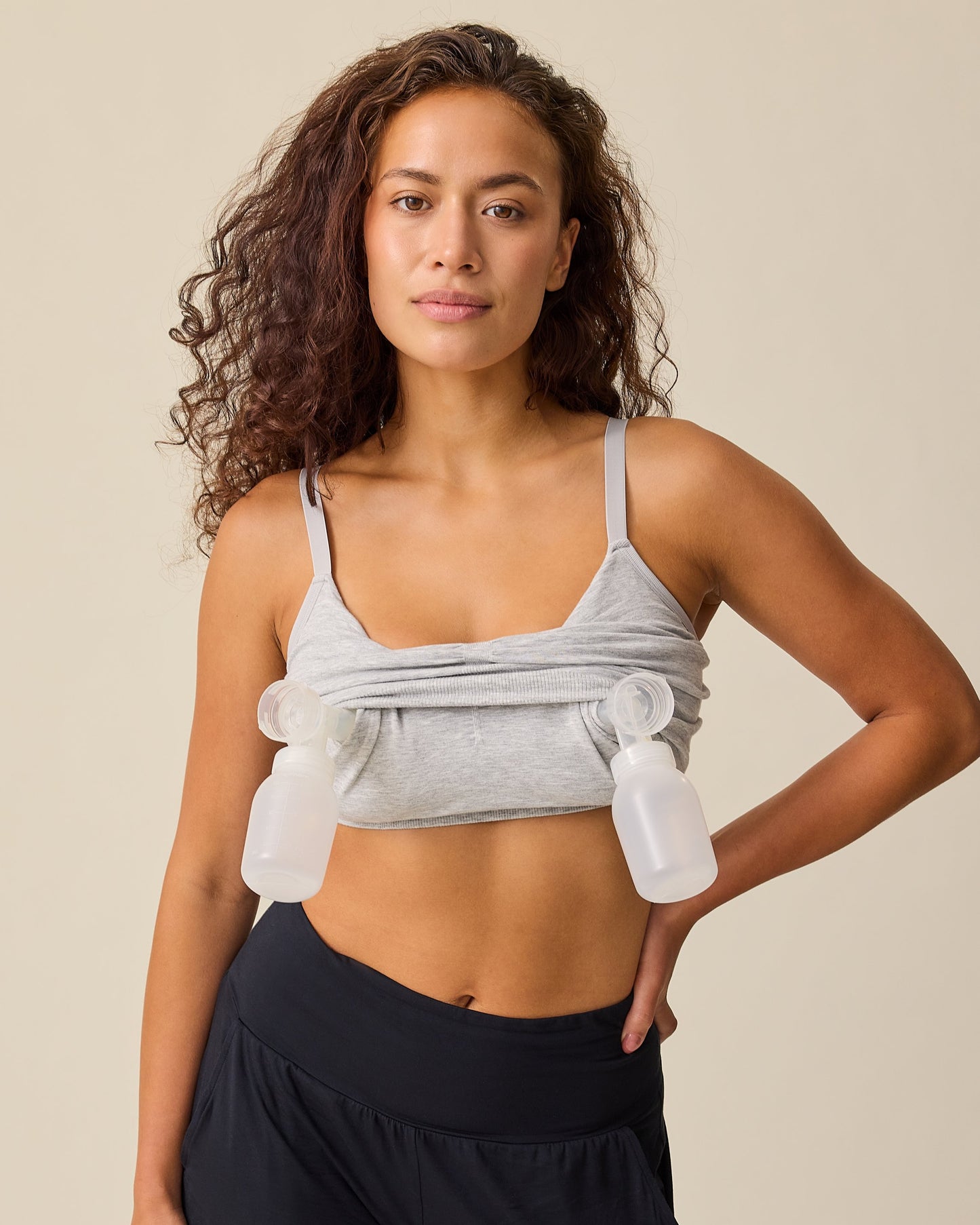Model is wearing Sublime® Bamboo Hands-Free Pumping Lounge & Sleep Bra in Grey Heather, while pumping, on a beige background.