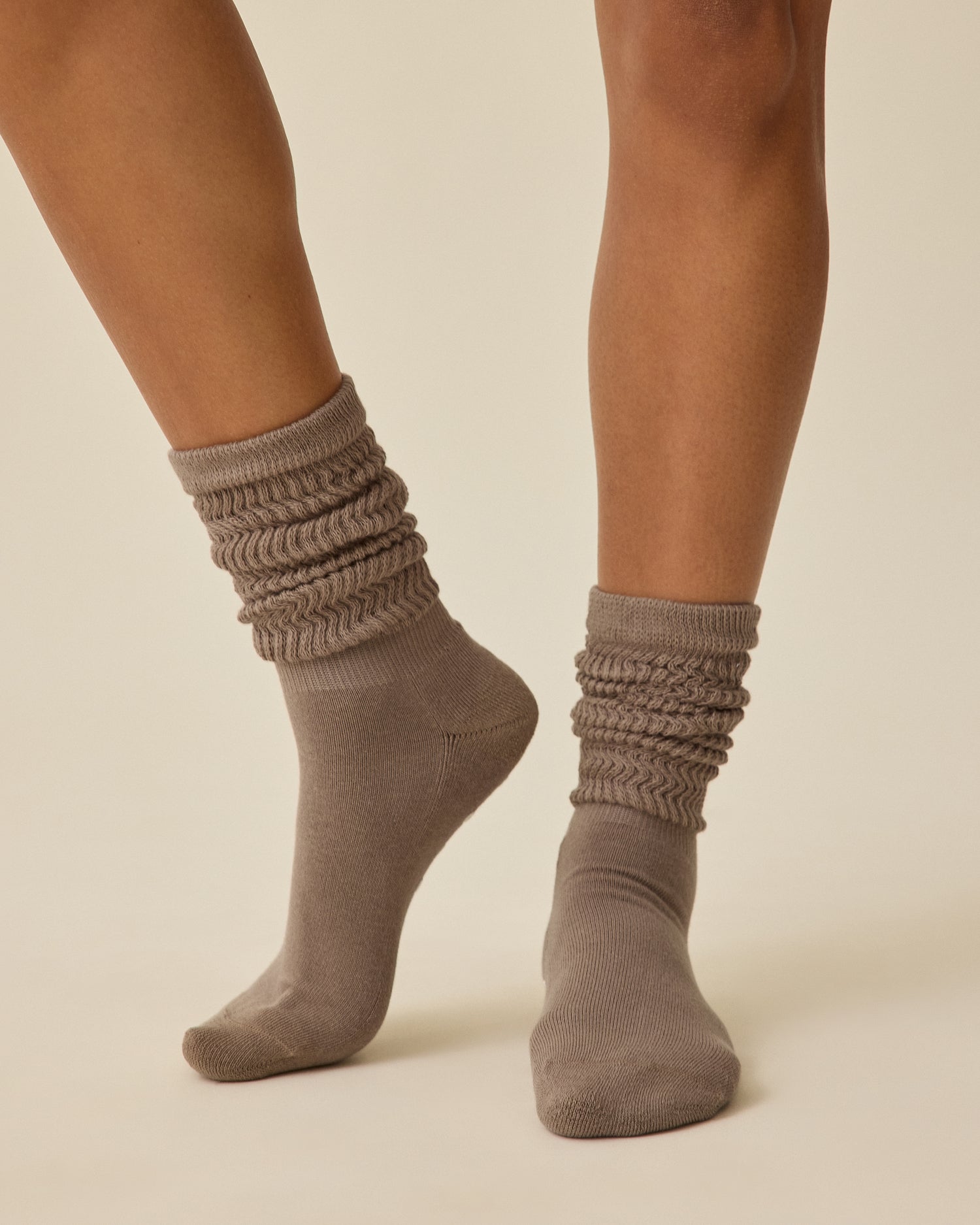 Model is wearing a pair of Non-Slip Slouchy Socks in Taupe on a beige background