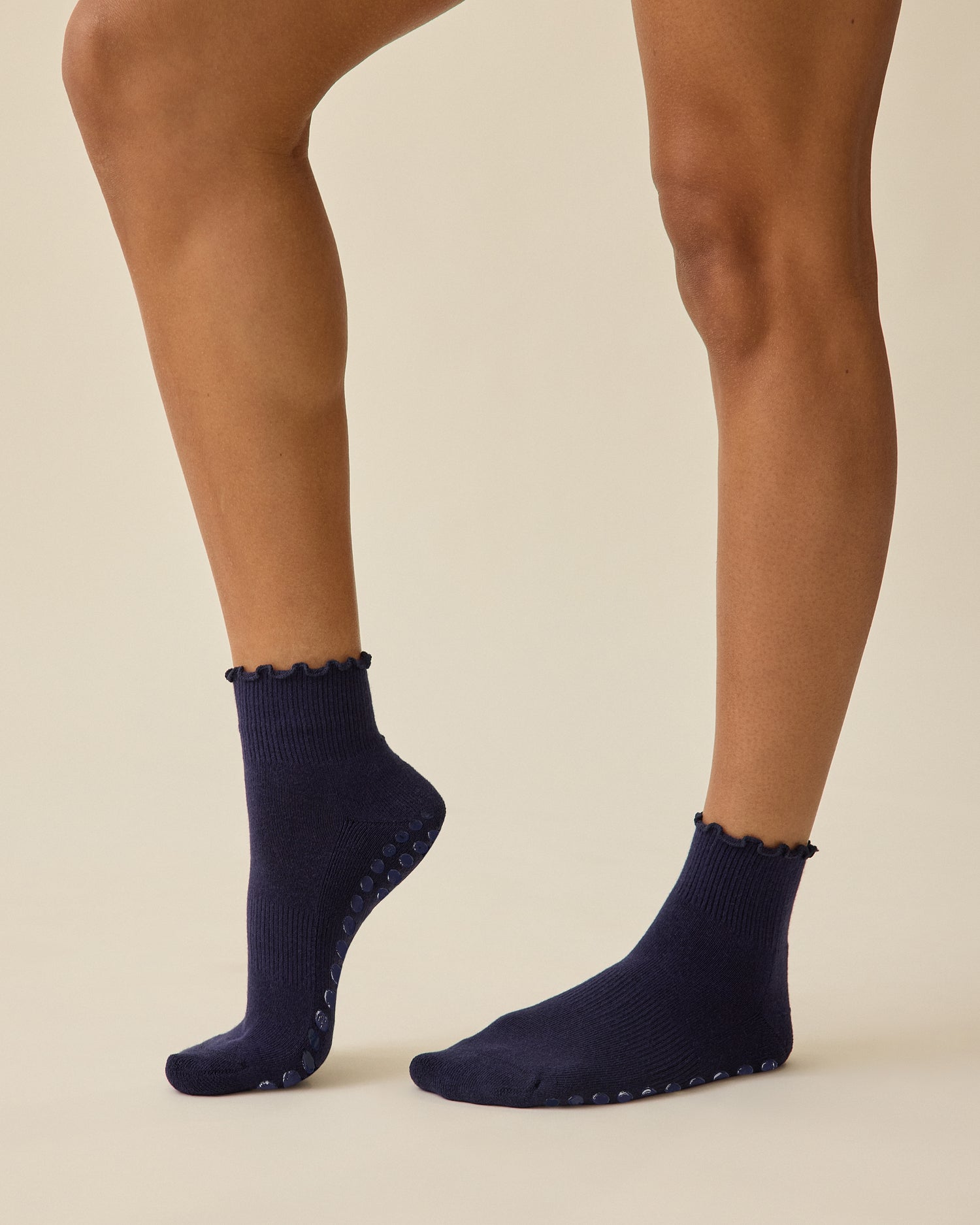 Model is wearing a pair of Non-Slip Ruffle Ankle Socks in Navy on a beige background.