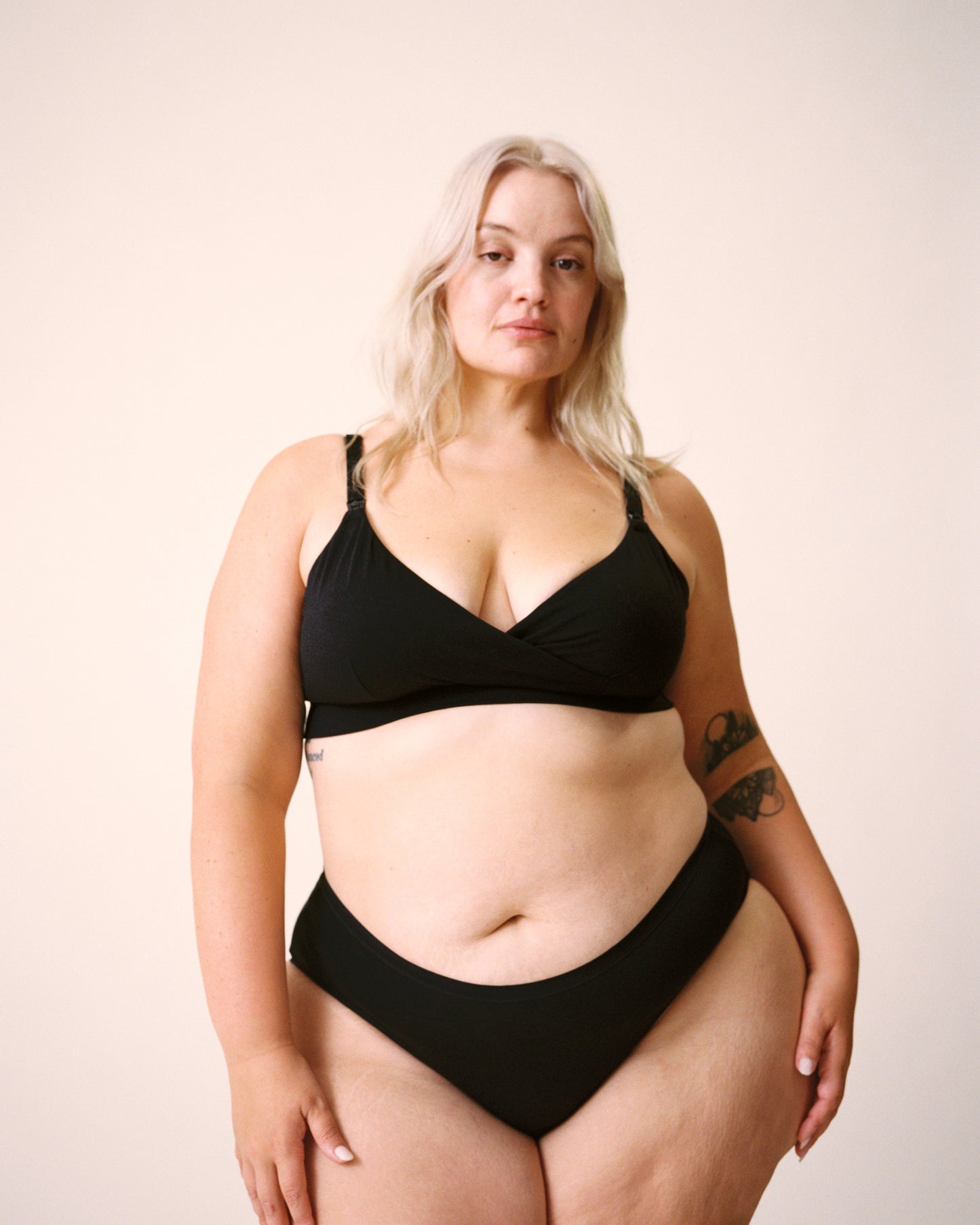 Blown out stylized image of model is wearing SoftStretch Cotton Nursing Bra and SoftStretch Cotton Maternity & Postpartum Hipster in Black on a beige background. 