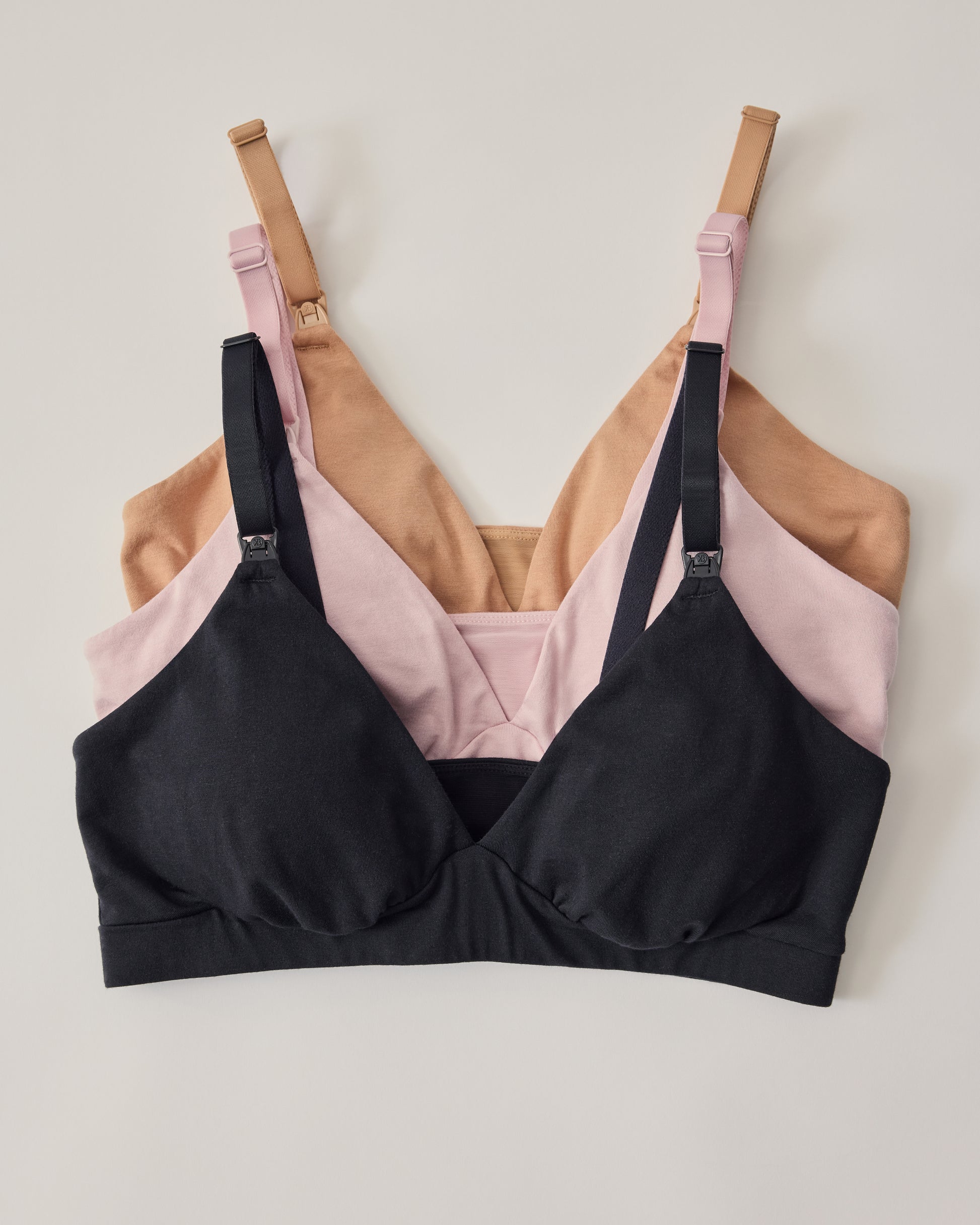 Flat lay of three SoftStretch Cotton Maternity & Nursing Bralettes in Buff, Lilac Mist and Black on a beige background.
