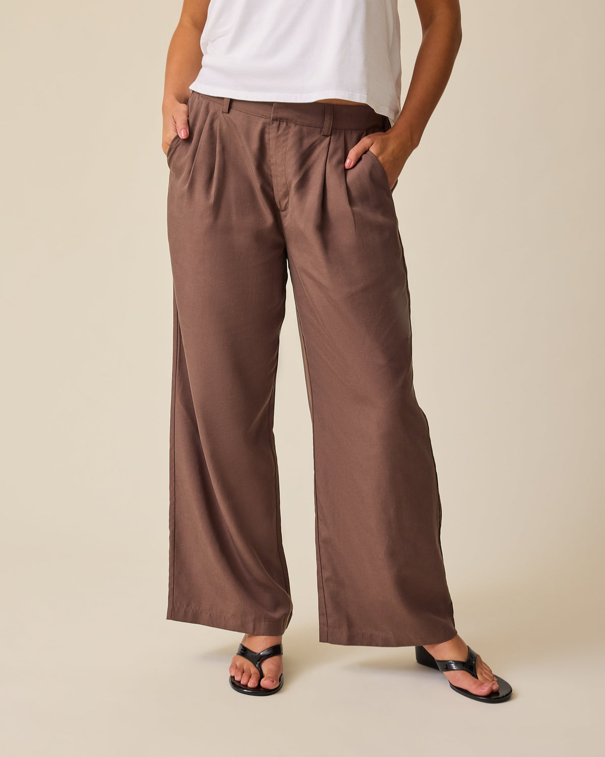 Model is wearing Maternity & Postpartum Wide Leg Trouser in Brown and Ruched Maternity Sleeveless Top in White, on a beige background.@model_info:Sadie is 5'8" and wearing a Medium.