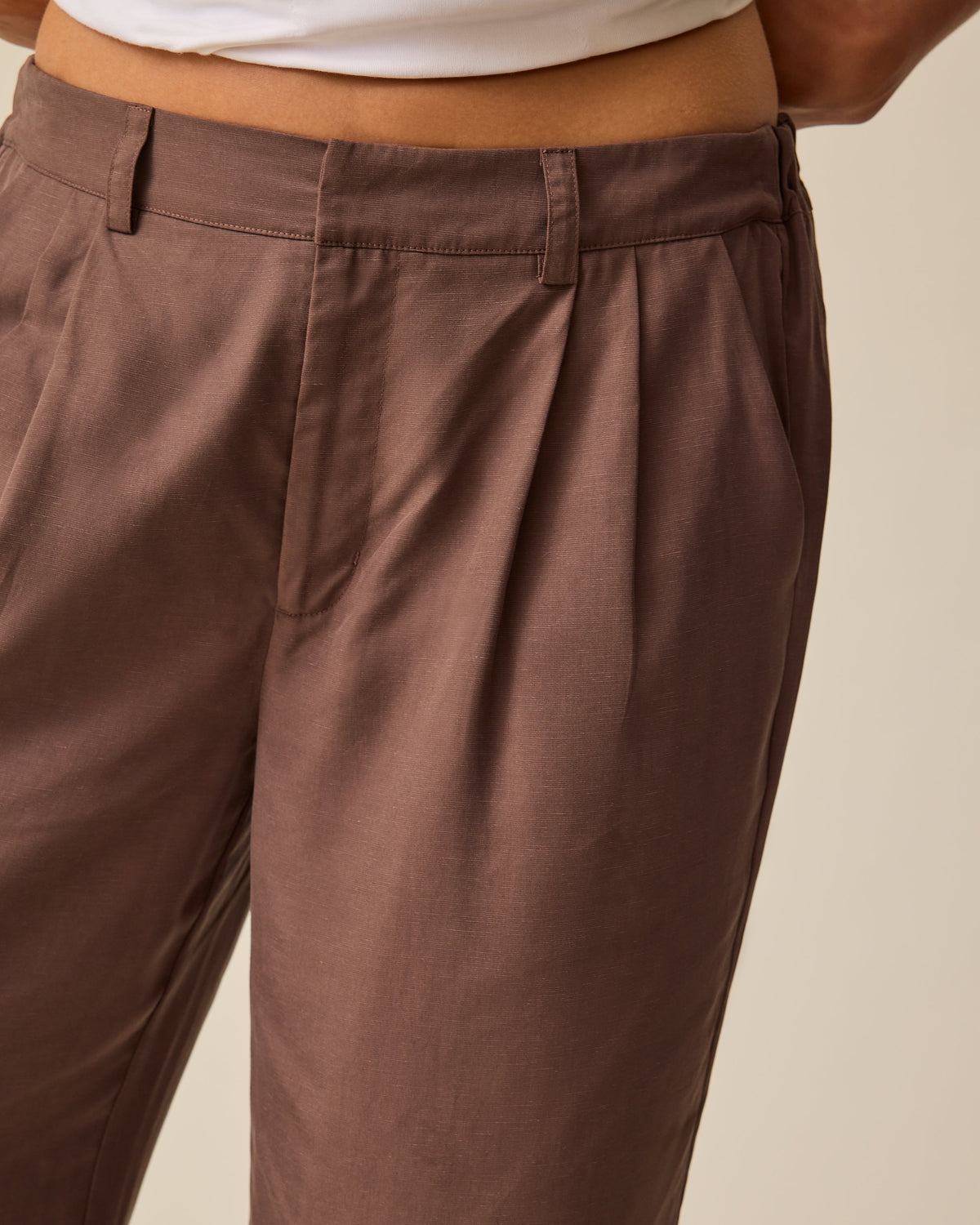 Model is wearing Maternity & Postpartum Wide Leg Trouser in Brown and Ruched Maternity Sleeveless Top in White, on a beige background.