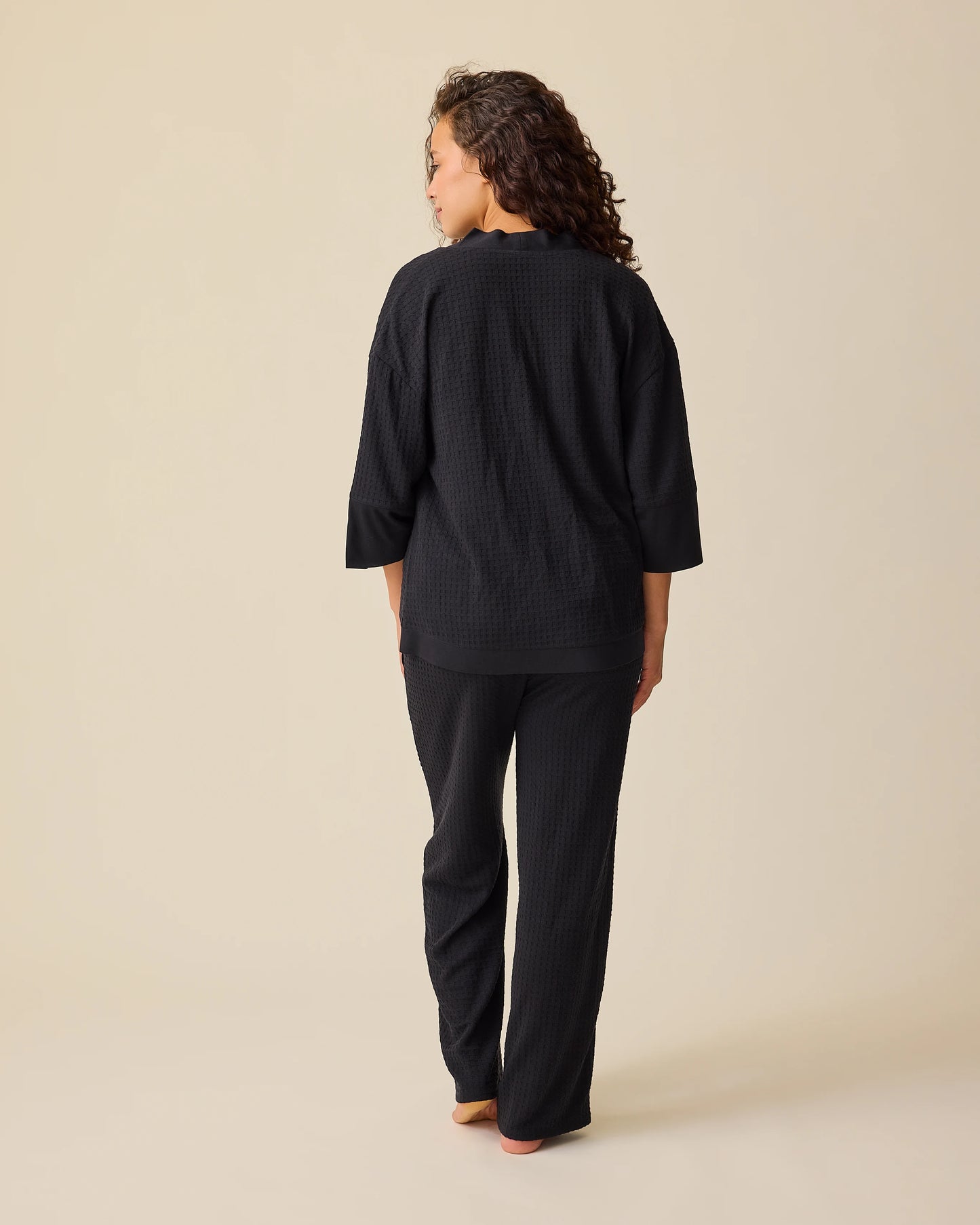 Back view of model wearing the Waffle Maternity & Nursing Three-Piece Lounge Set in Black on a beige background. 
