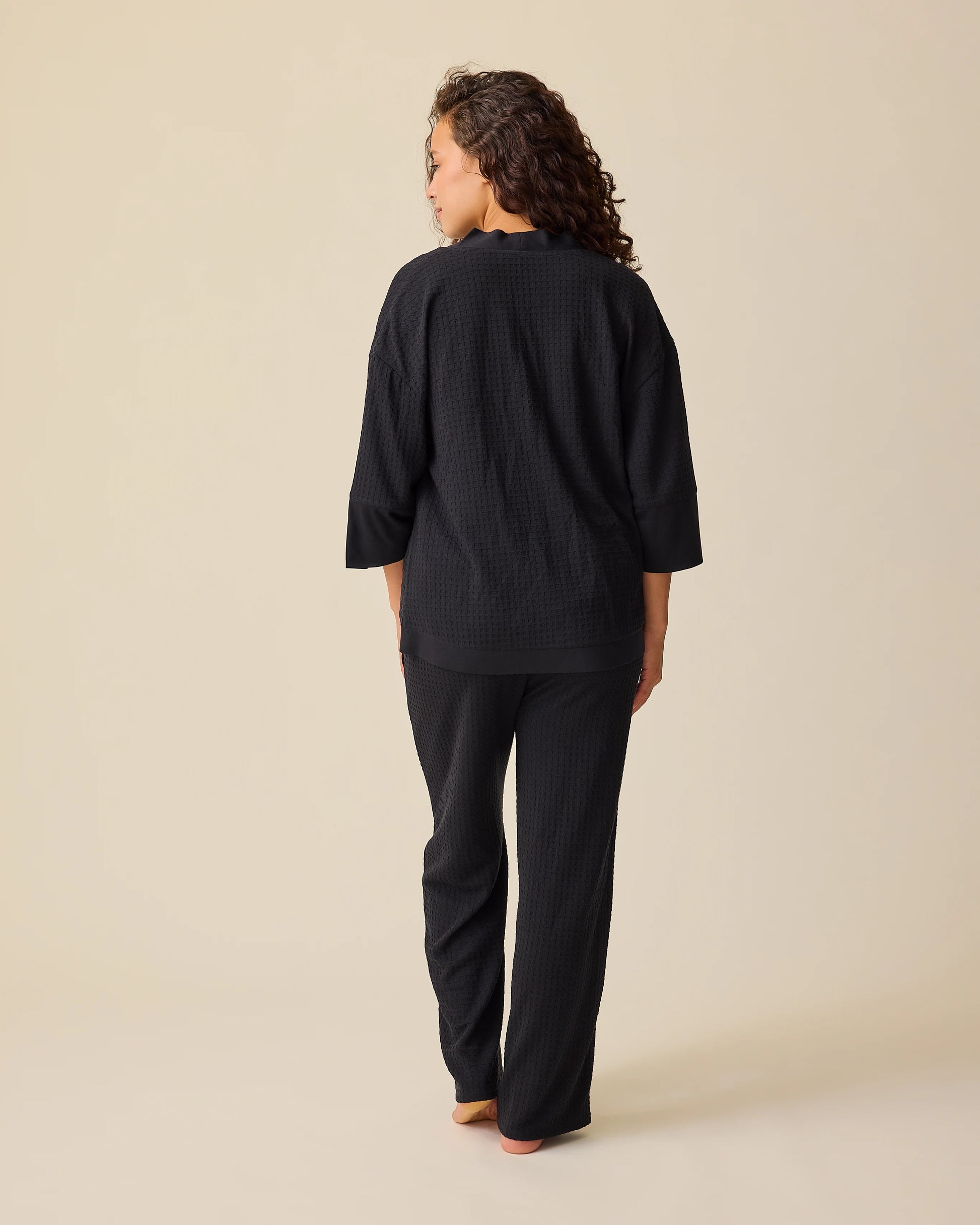 Back view of model wearing the Waffle Maternity & Nursing Three-Piece Lounge Set in Black on a beige background. 