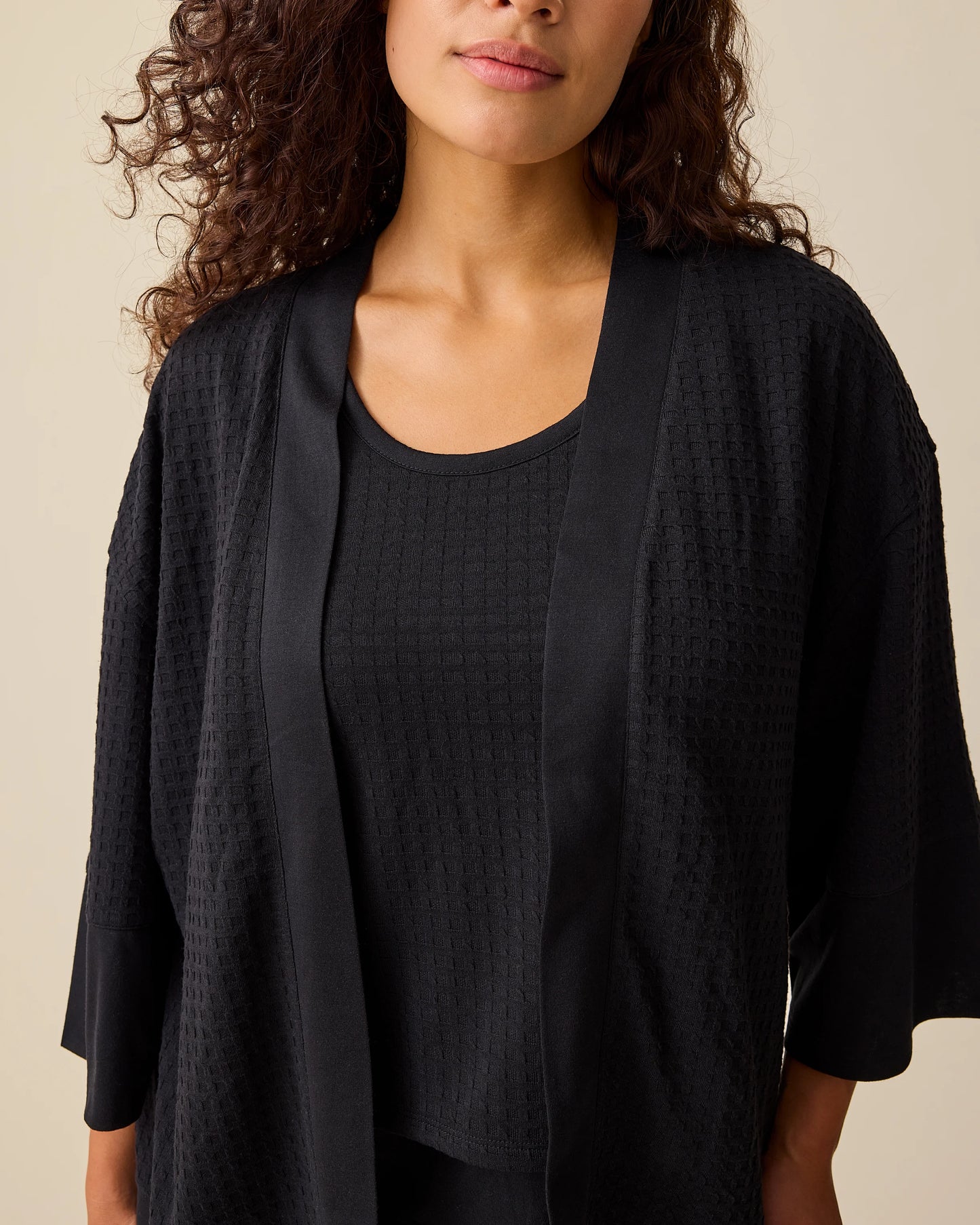 Close up of the model wearing the Waffle Maternity & Nursing Three-Piece Lounge Set in Black on a beige background. 
