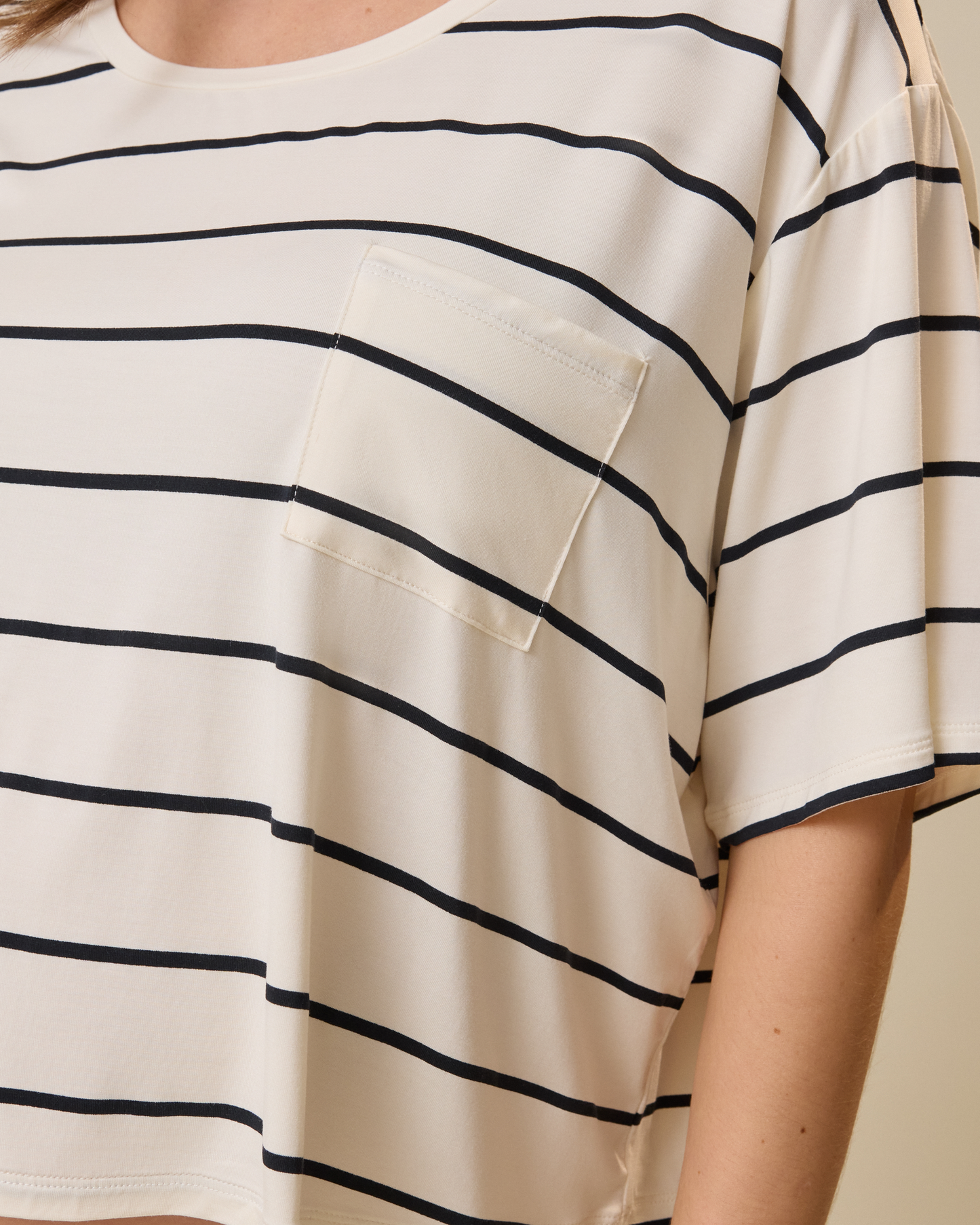 Close-up of a person wearing a white t-shirt with black horizontal stripes on a beige background