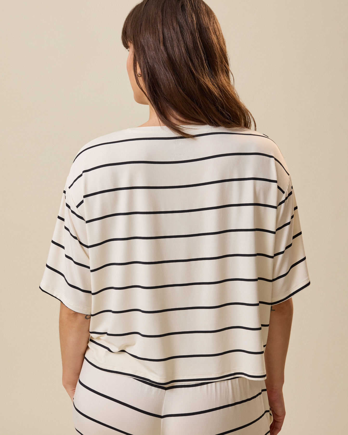 Person wearing a white and black striped short sleeve lounge shirt on a beige background