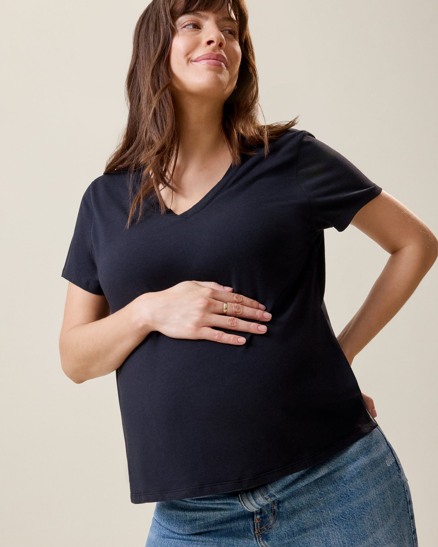 Front view of model wearing Classic Modal V-neck Nursing T-shirt in Black with a hand placed over her pregnant belly@model_info:KJ is wearing a Medium.