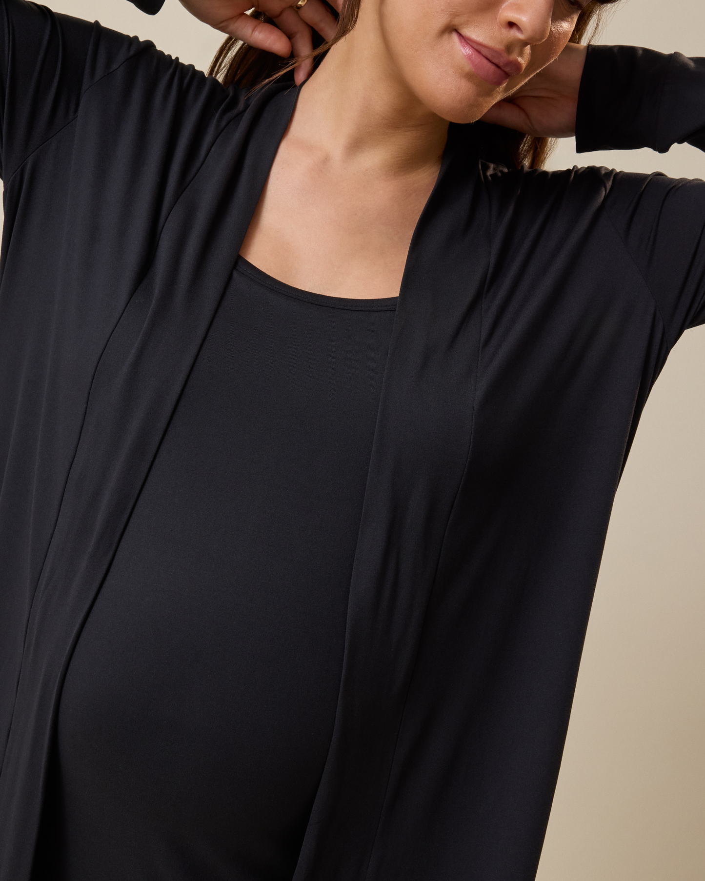 Person wearing a black long-sleeve duster with a beige background