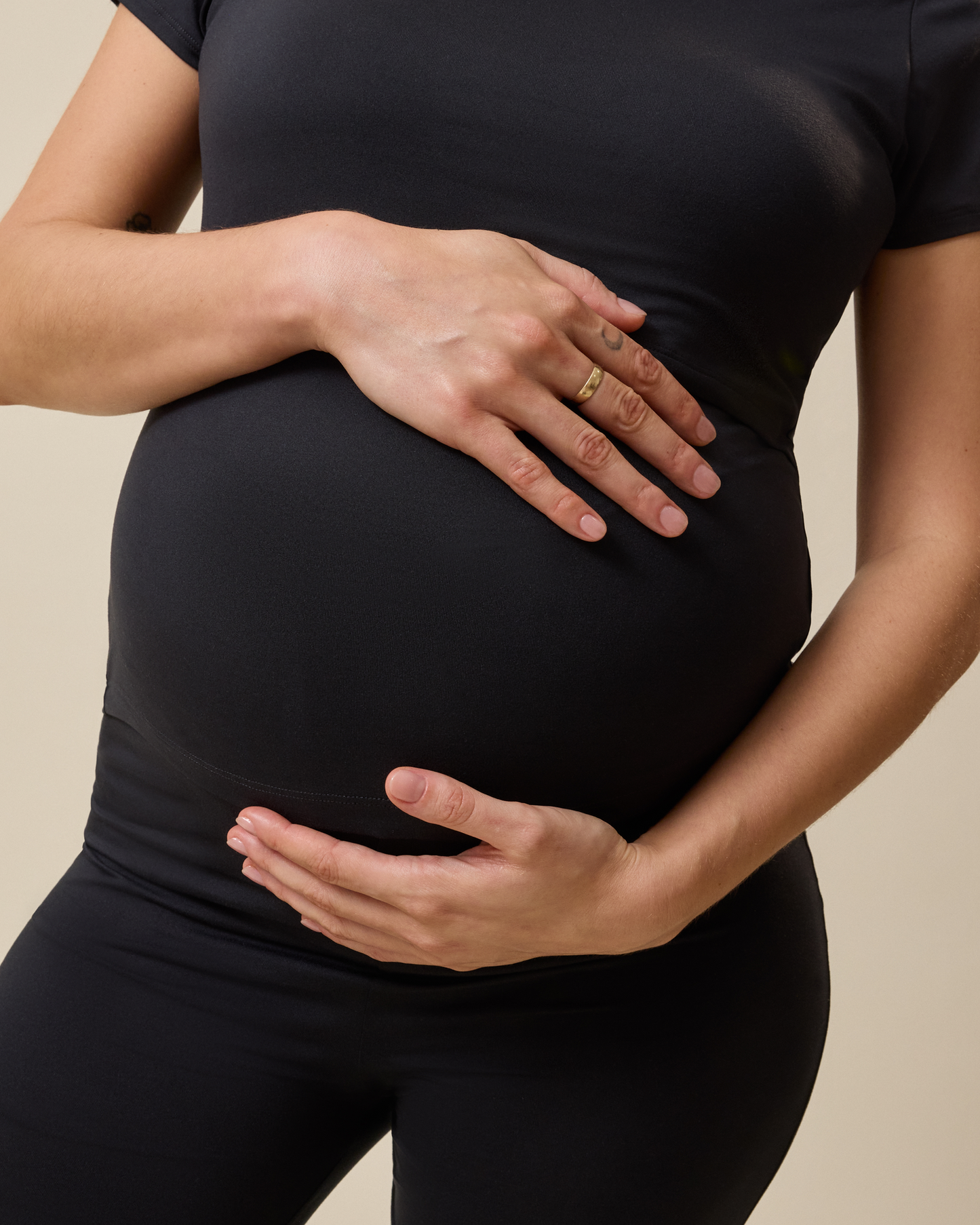 Pregnant person wearing a black outfit with hands on belly a beige background