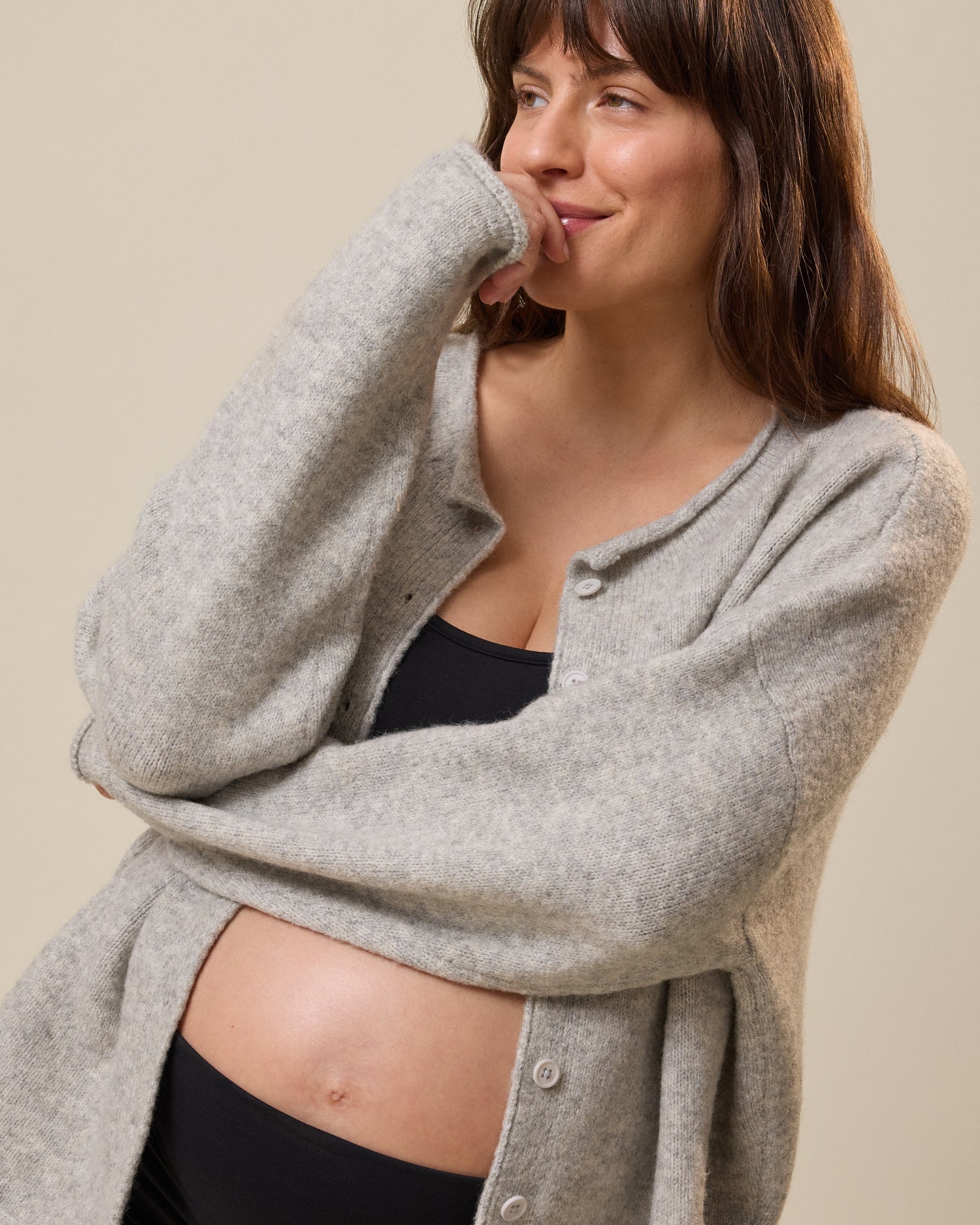 Woman wearing a gray cardigan over a black bra against a beige background