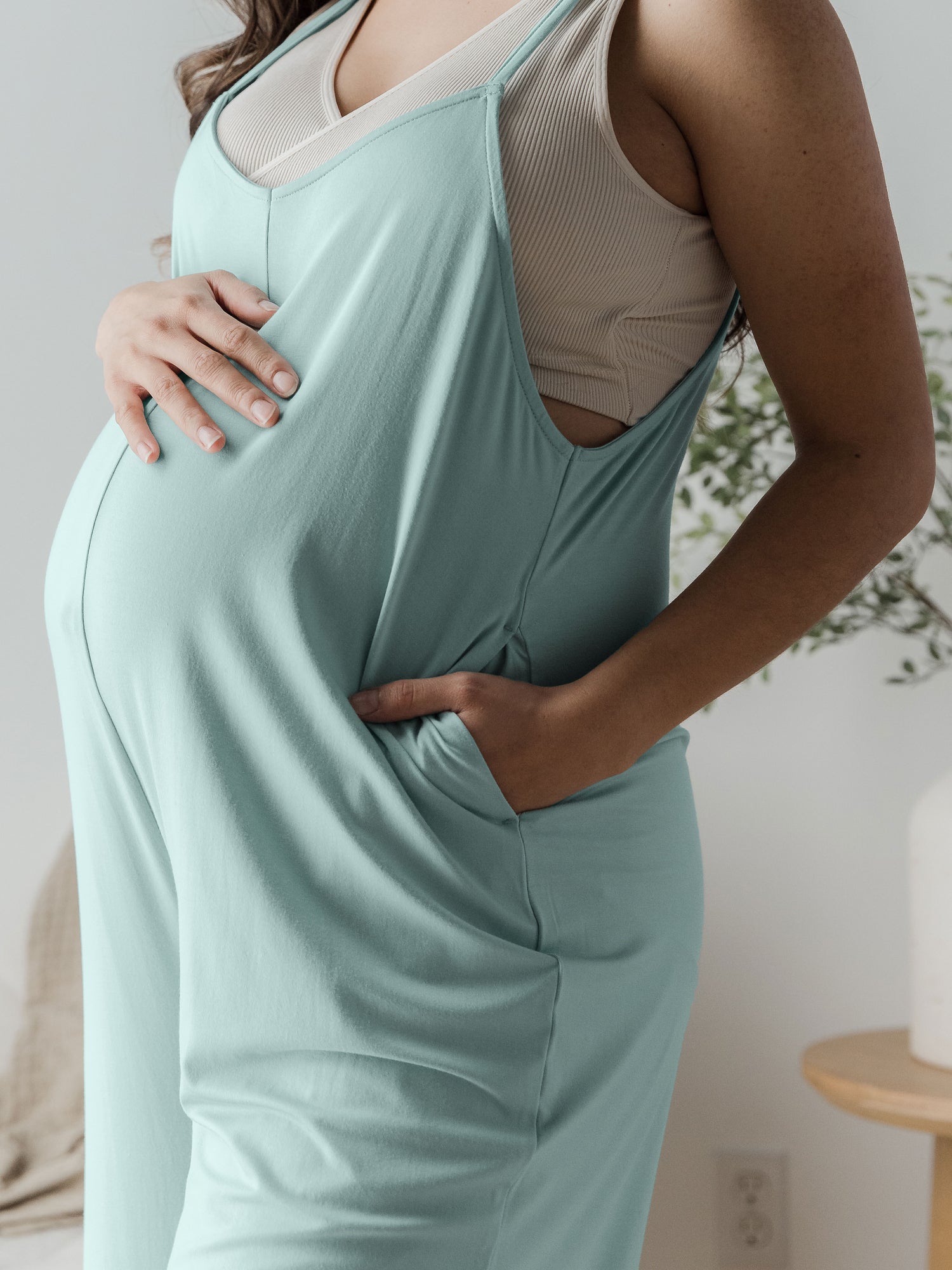 Closeup of a pregnant model wearing the Charlie Maternity & Nursing Romper in Dusty Blue Green with hand in pocket and on belly bump.