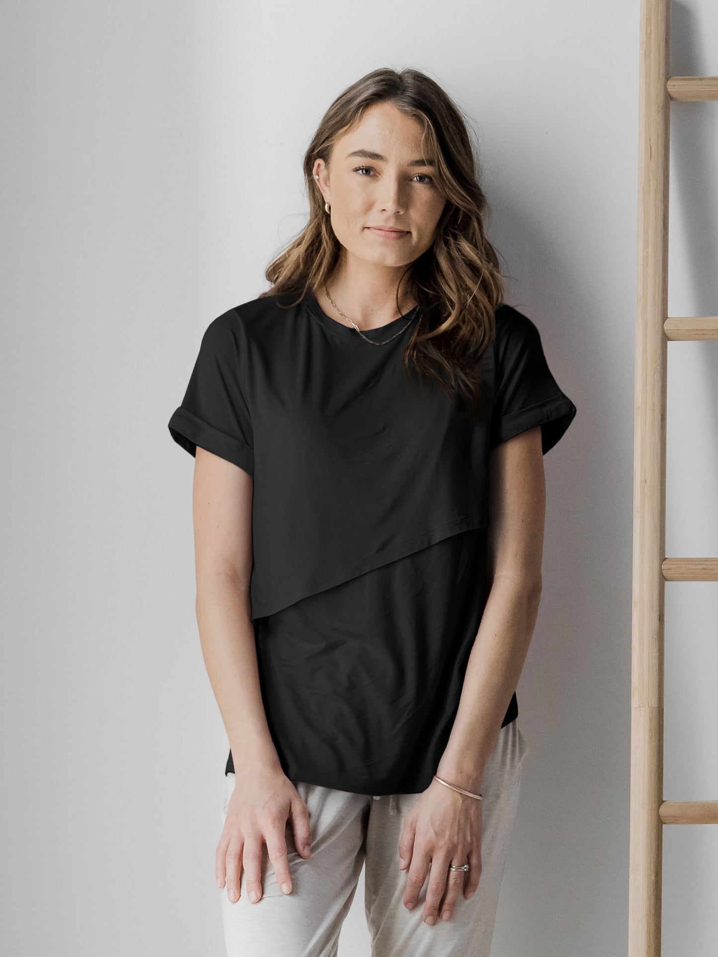Model standing against the wall wearing the Everyday Asymmetrical Nursing T-Shirt in Black